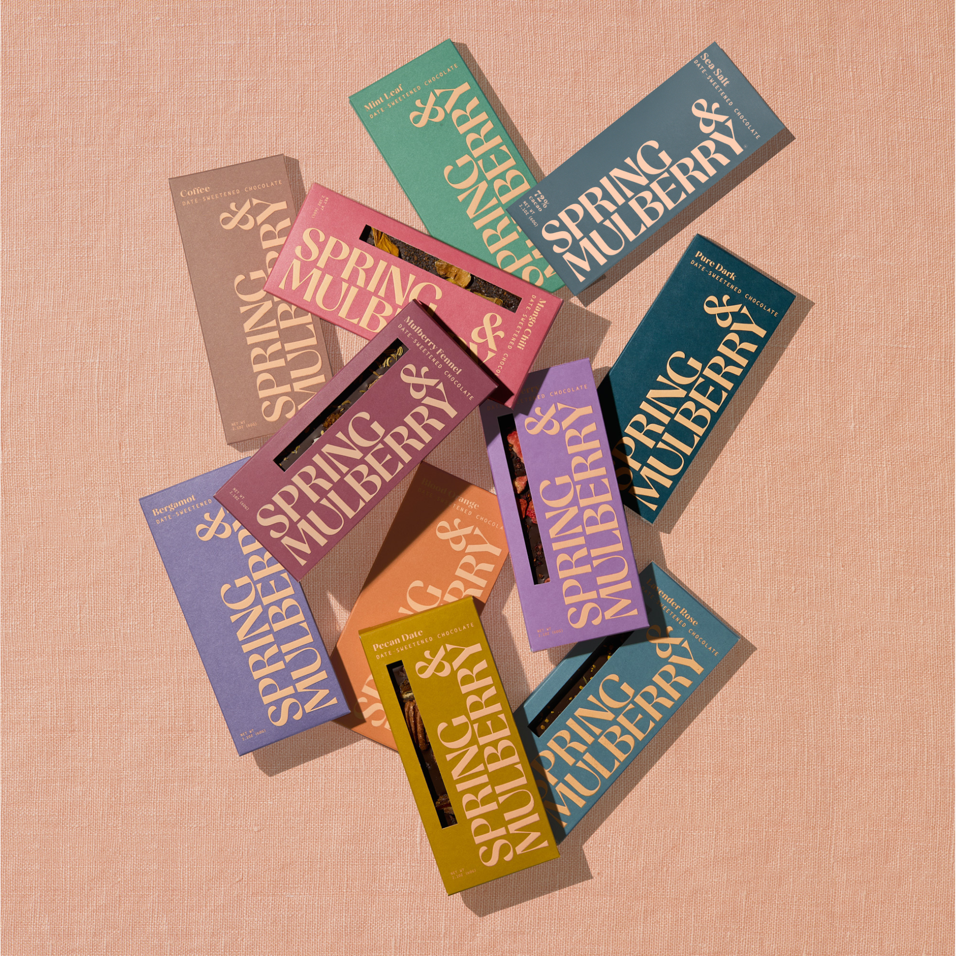 All 11 artisanal chocolate bars in their Spring & Mulberry boxes are laid out on a surface, each with different color packaging representing various flavors.