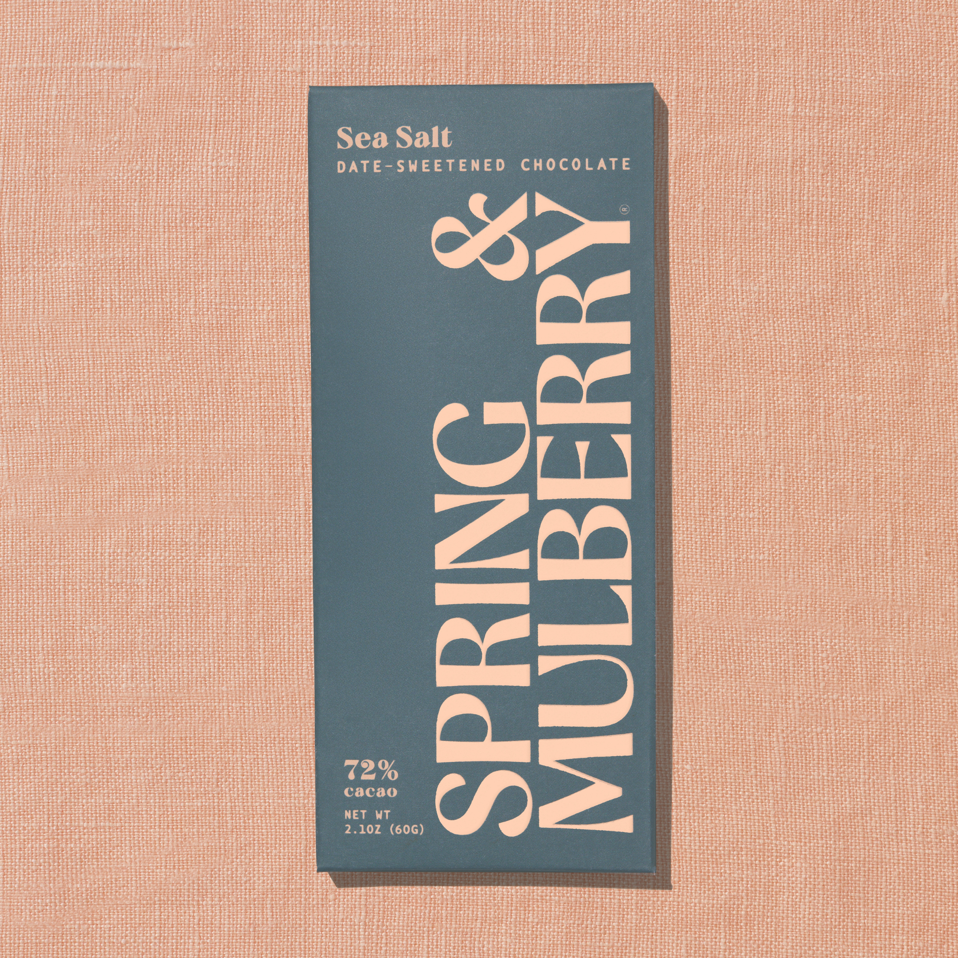 A grey Spring & Mulberry box labeled Sea Salt date-sweetened chocolate is laid on a light peach background.