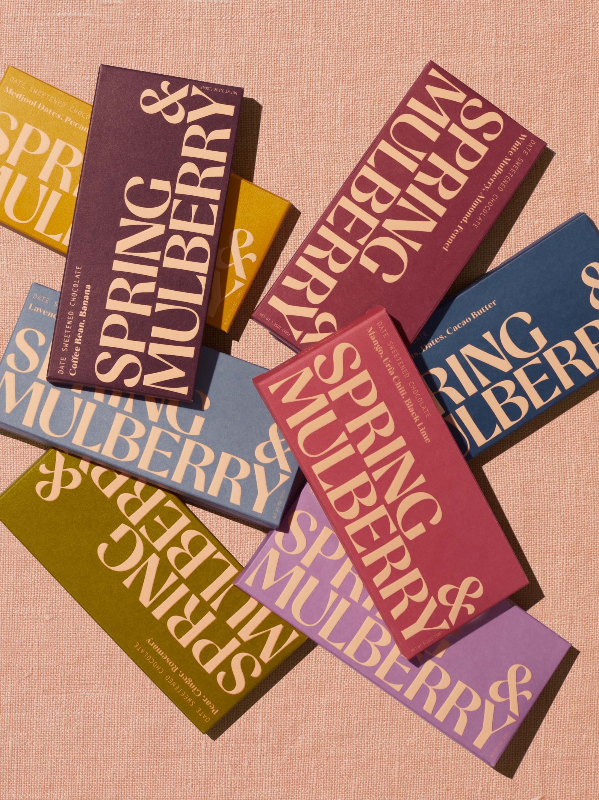 All eight of Spring & Mulberry's date-sweetened chocolate bars with no added sugar sit in two rows upon a peach linen backdrop.