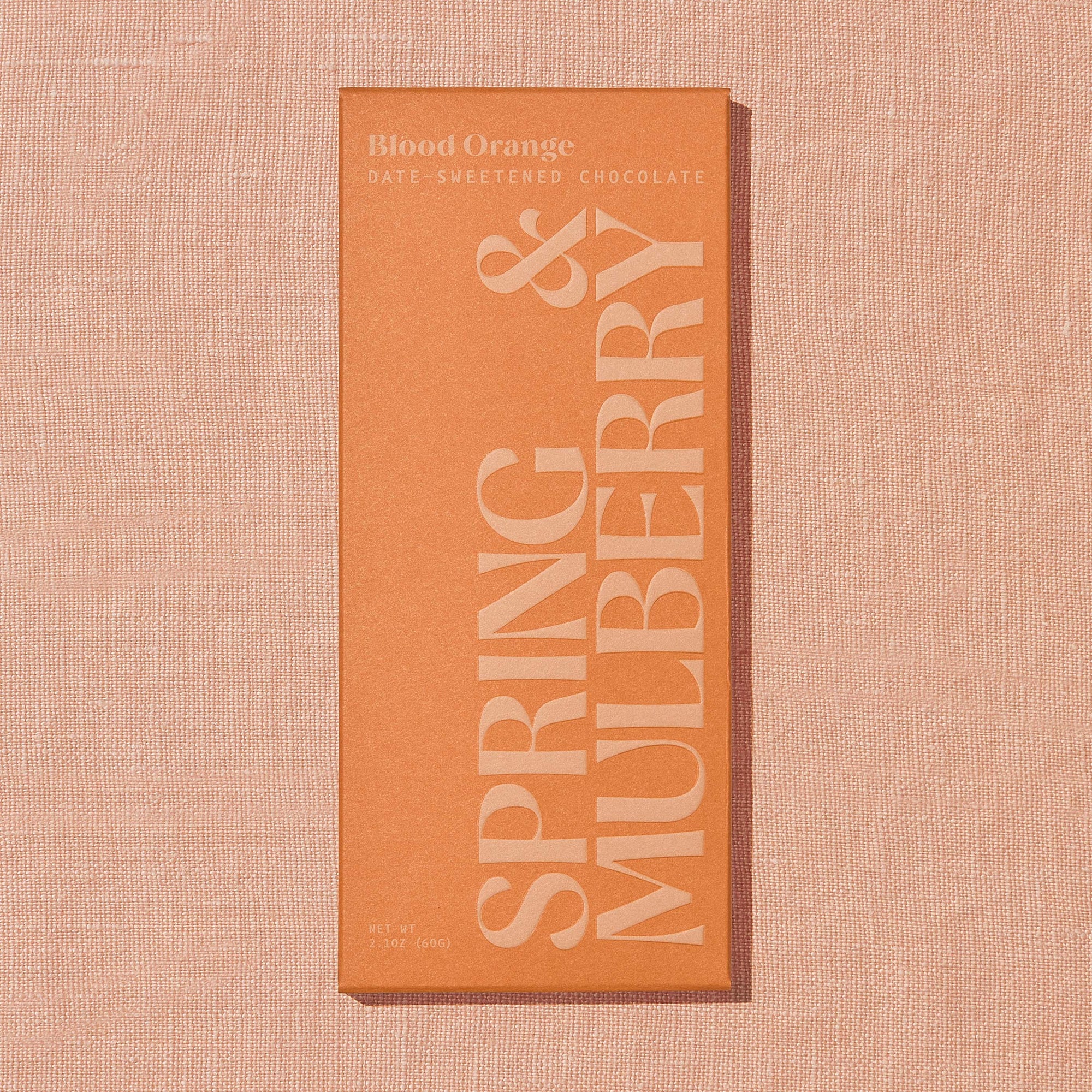 A bright orange Spring & Mulberry box labled Blood Orange date-sweetened chocolate on a warm brown background.