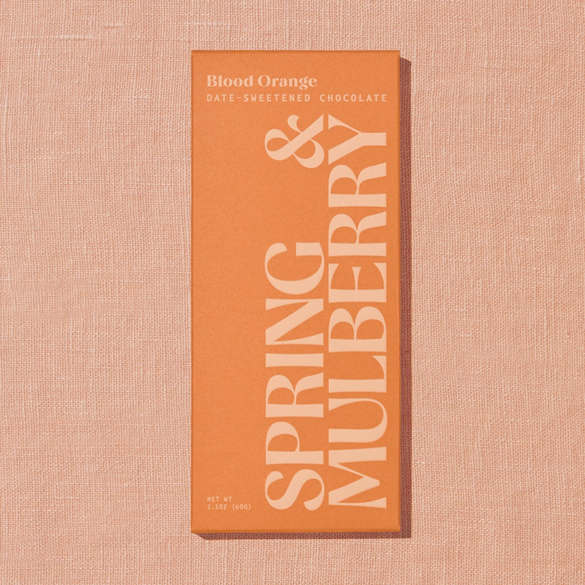 A light orange Spring & Mulberry box labled Blood Orange date-sweetened chocolate is laid on a warm brown background.