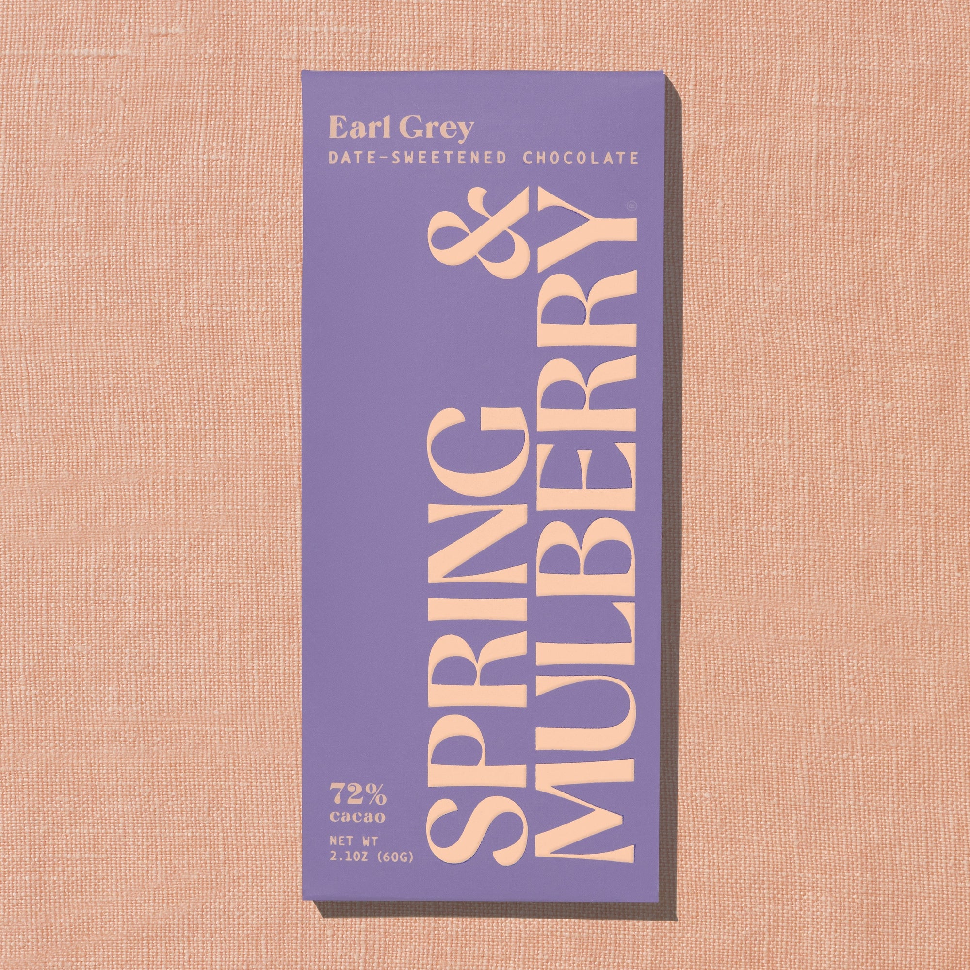 A light purple Spring & Mulberry box labled Earl Grey date-sweetened chocolate is laid on a warm brown background.