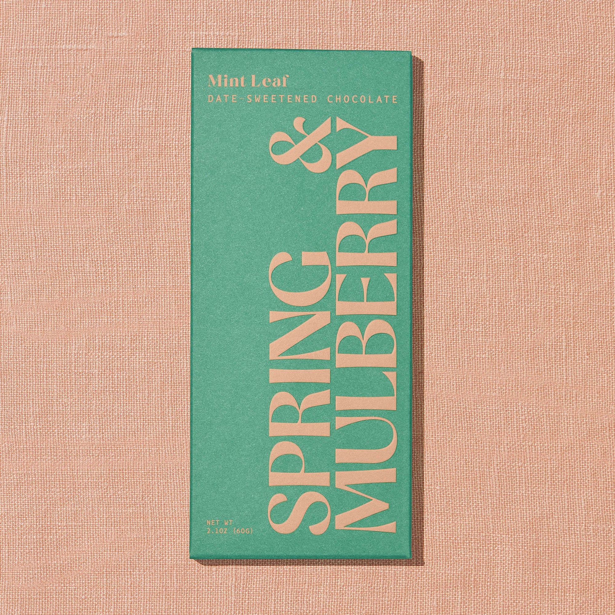 A light green Spring & Mulberry box labled Mint Leaf date-sweetened chocolate on a warm brown background.