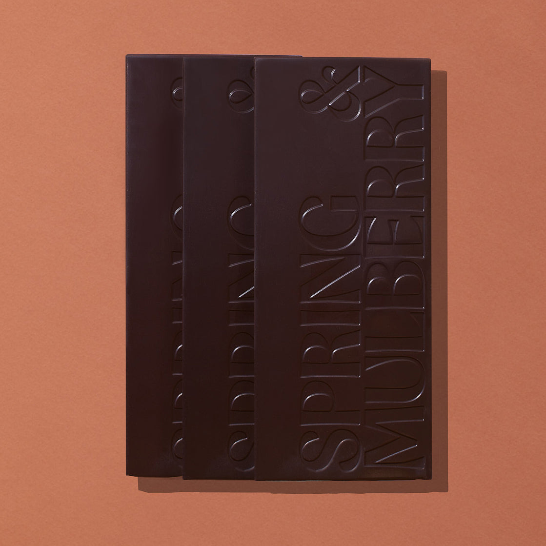 A set of three artisanal chocolate bars infussed with essential oils and stamped with our Spring & Mulberry logo layed out flat on a warm brown background.