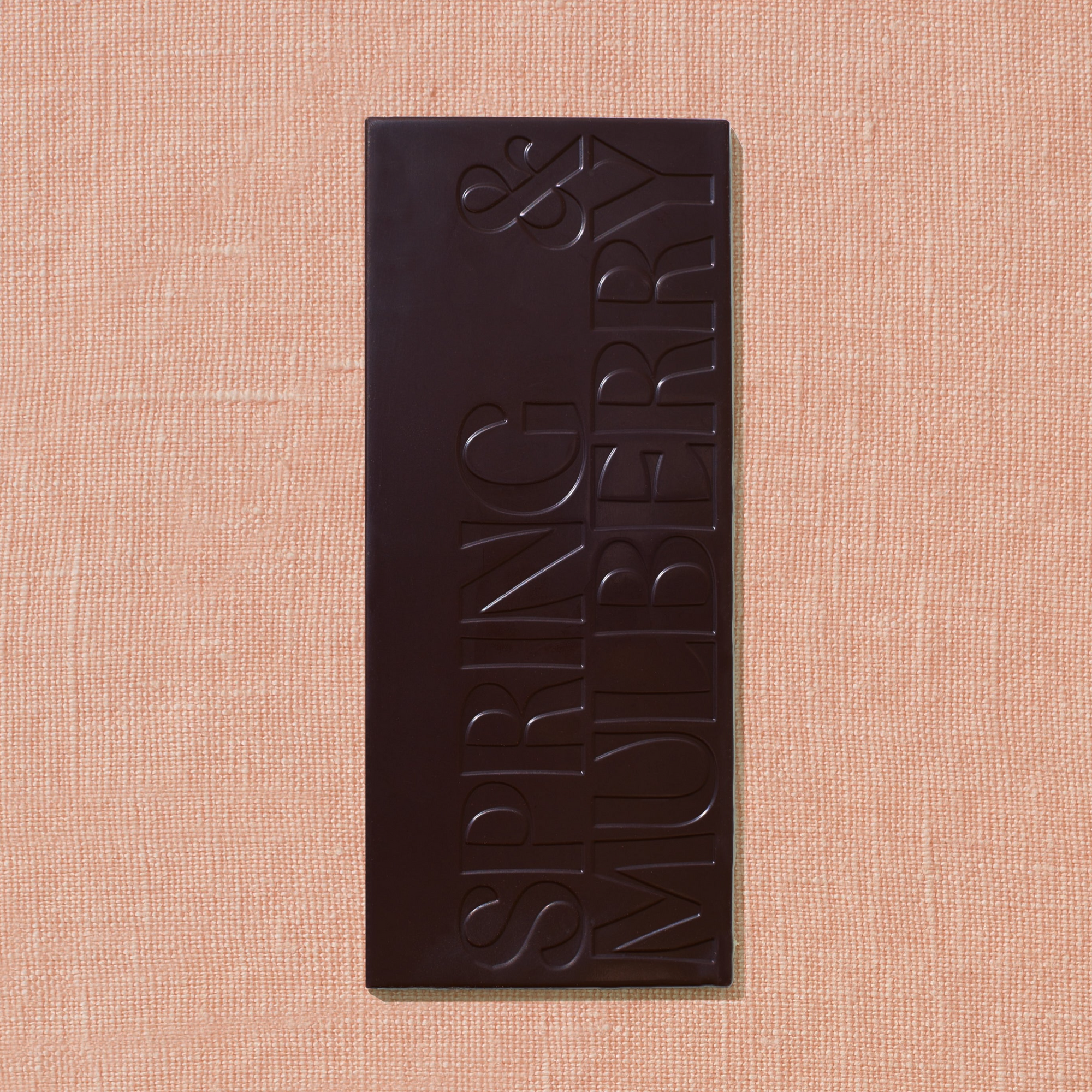 One chocolate bar that is stamped with Spring & Mulberry logo and infused with sea salt flakes is laid out on a light peach background.