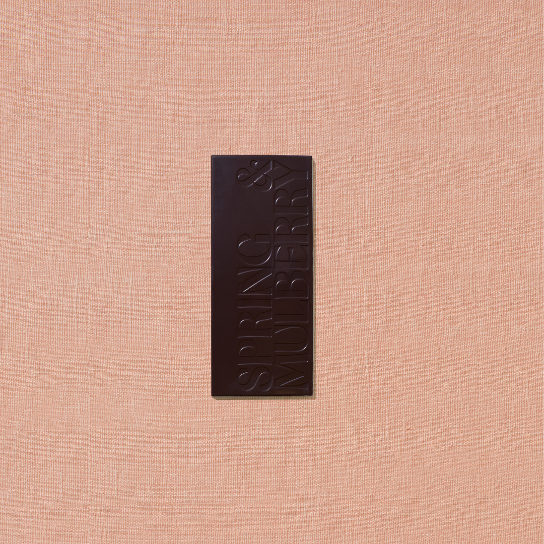 One small chocolate bar that is stamped with Spring & Mulberry logo is laid out on a warm brown background.
