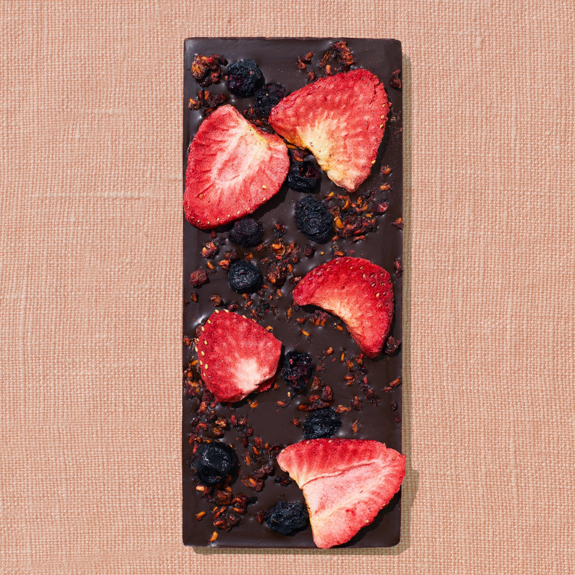 One chocolate bar that is topped with strawberries, blueberries, and red raspberries is laid out on a warm brown background.