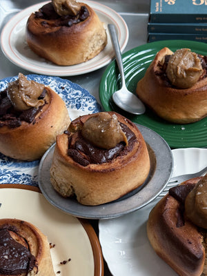 In this picture, there are six rolls, topped with chocolate and sea salt. Each in placed on a different colored plate. In the corner, there are 3 Spring & Mulberry Sea Salt bars. 