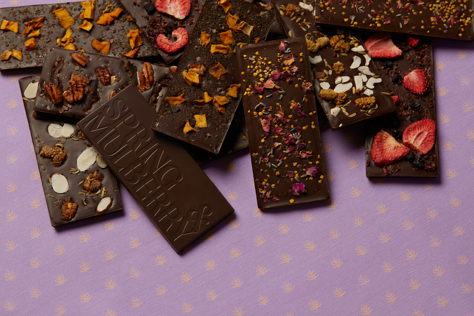 Five Spring & Mulberry date-sweetened chocolate bar boxes lay askew on a holiday table with oysters and fruit.