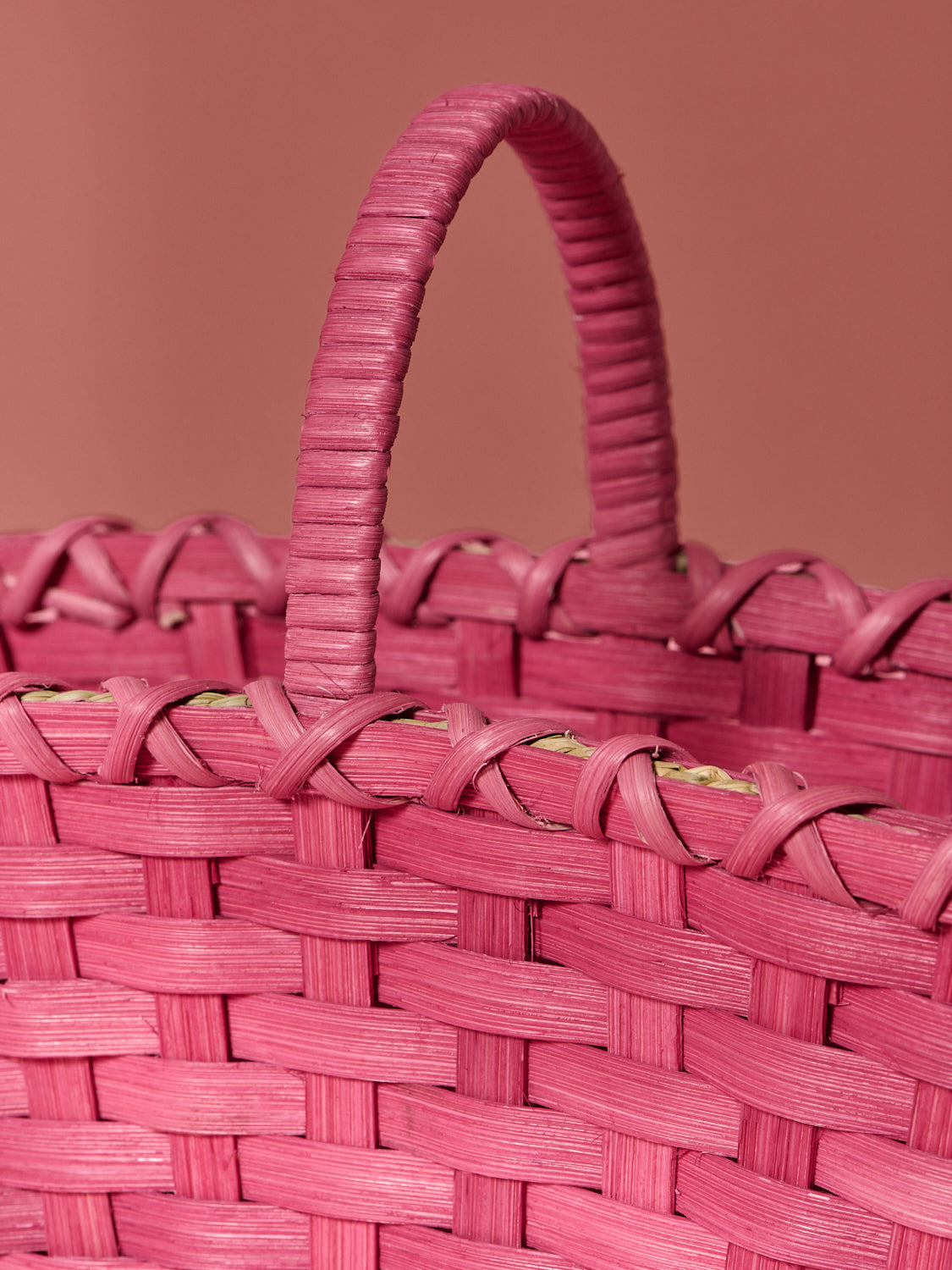 Close-up of a mulberry woven basket with handle on a matching pink 