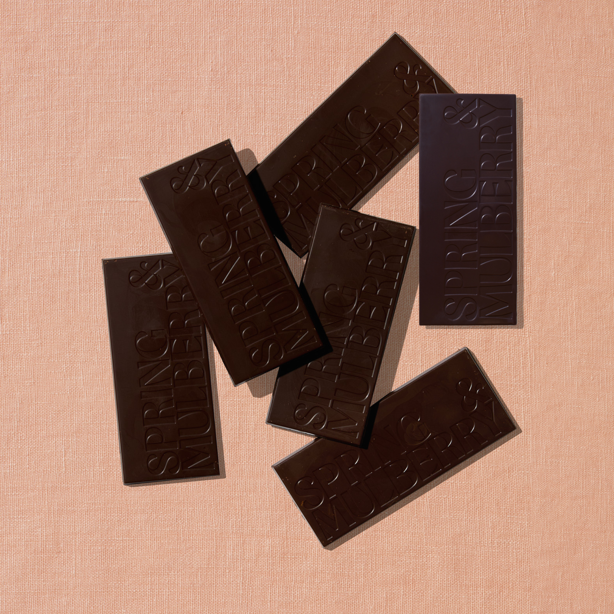 Five chocolate bars infused with essential oils, are laid out sparadically on a warm brown background.