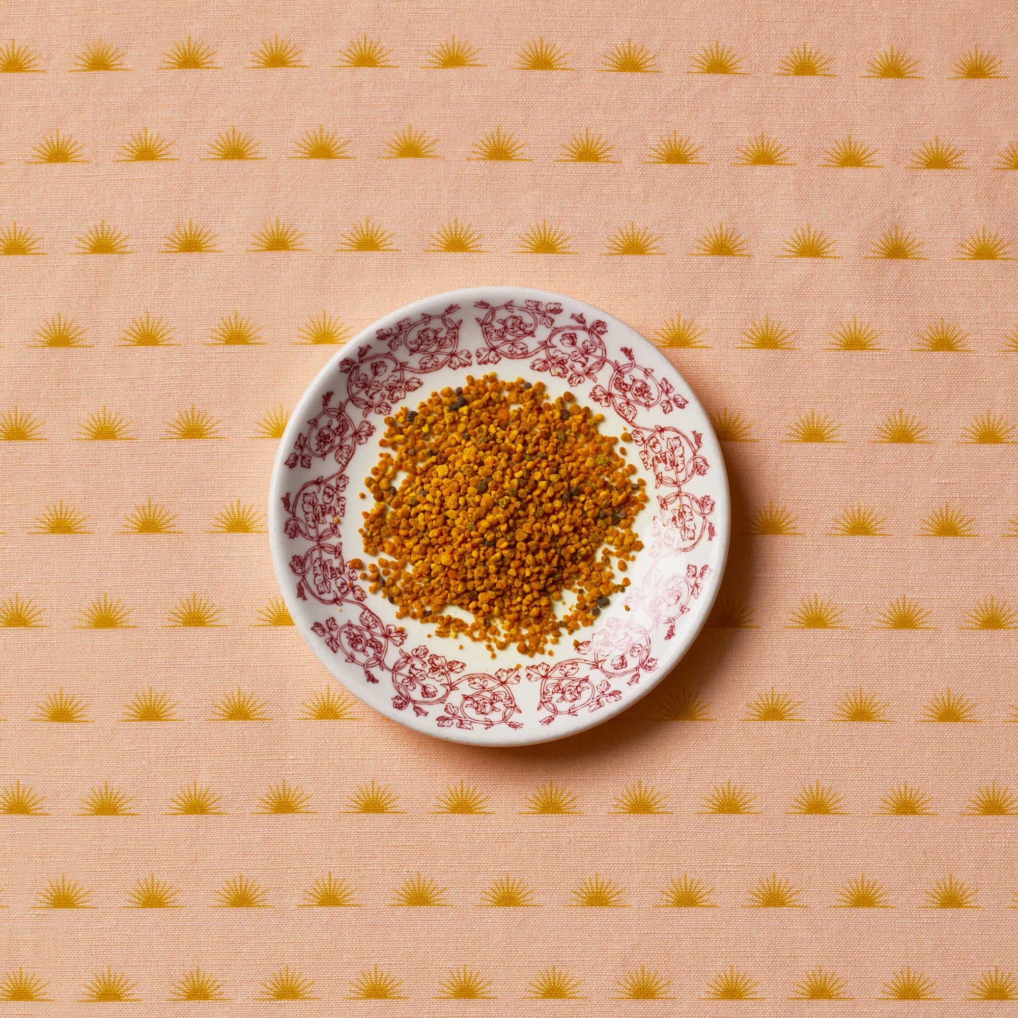 Bee pollen sitting on a white floral plate on top of a patterned tablecloth