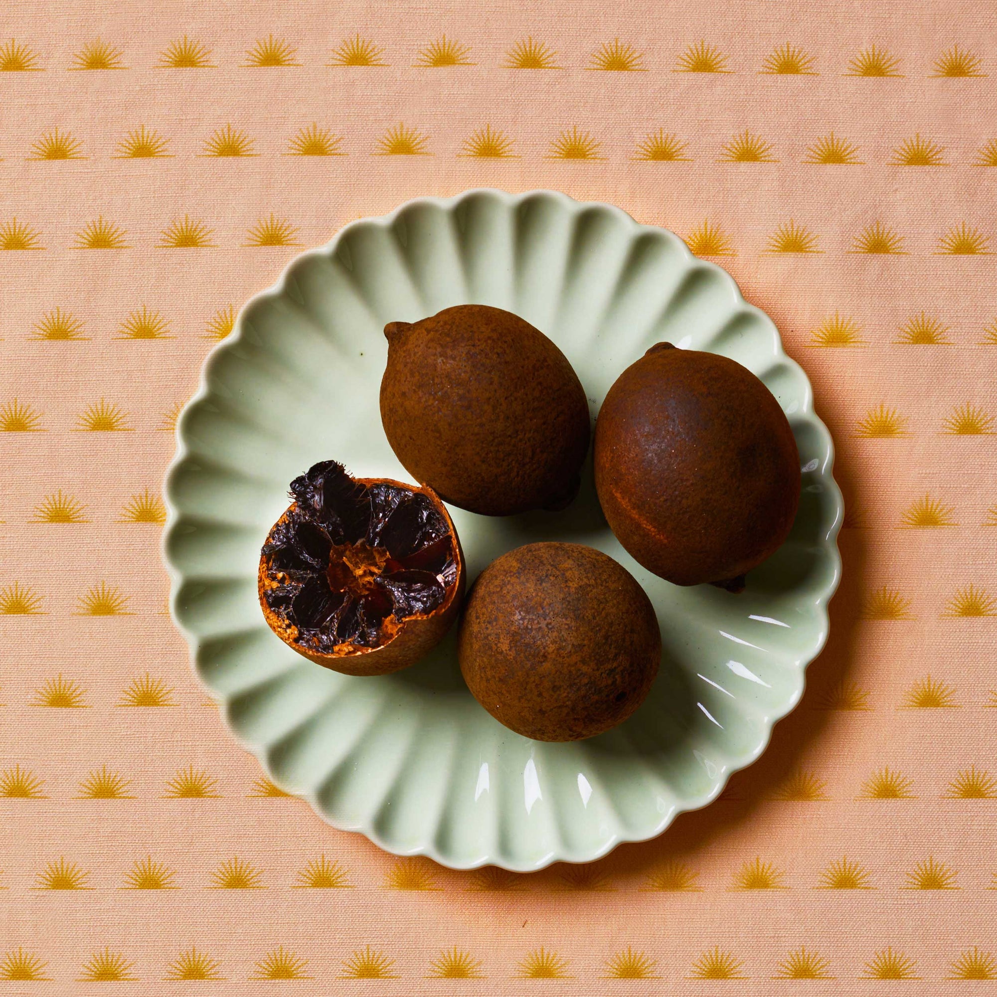 Black lime sitting on a mint scalloped plate on top of a patterned tablecloth