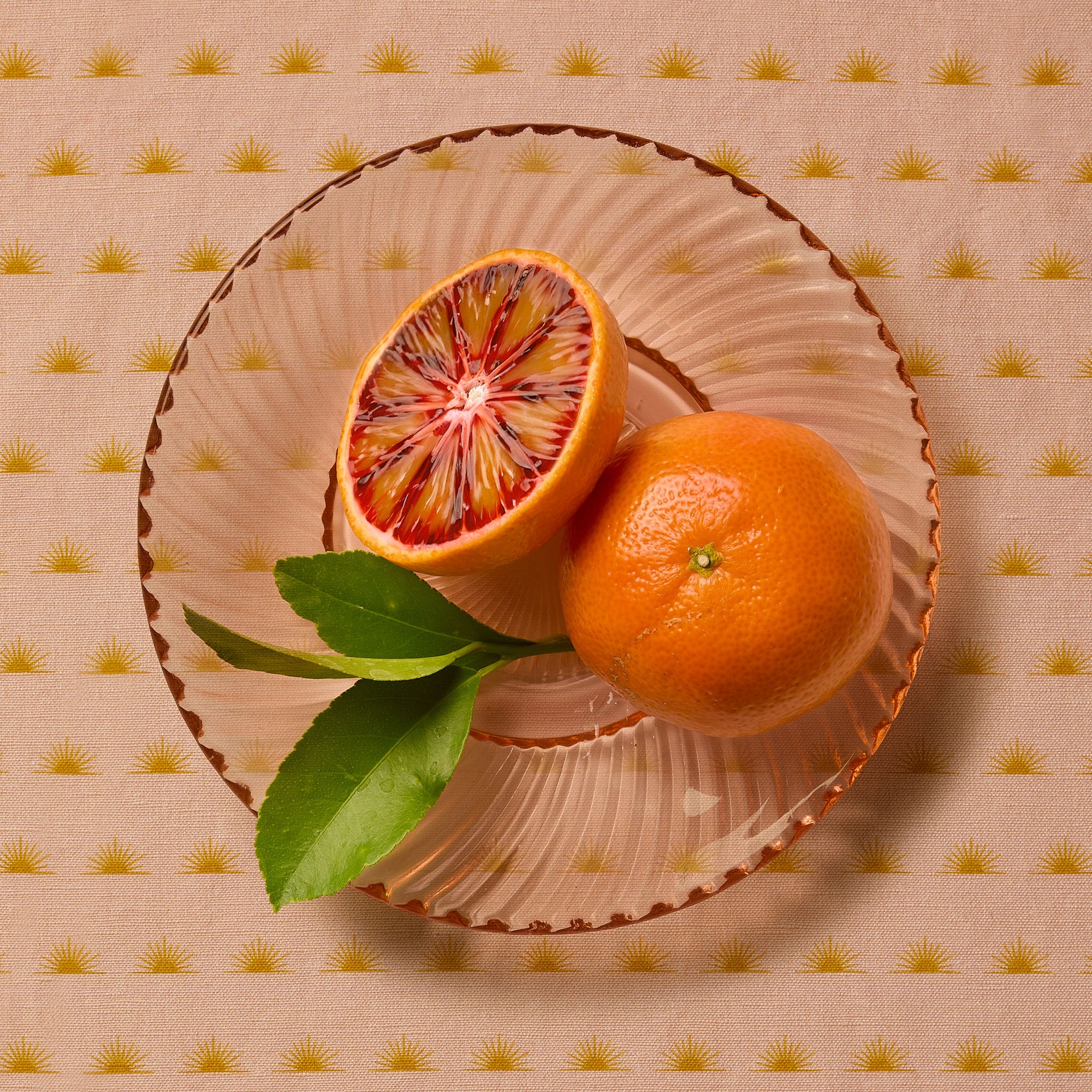 Blood Orange in a bowl in a rose colored glass bowl on a patterned tablecloth