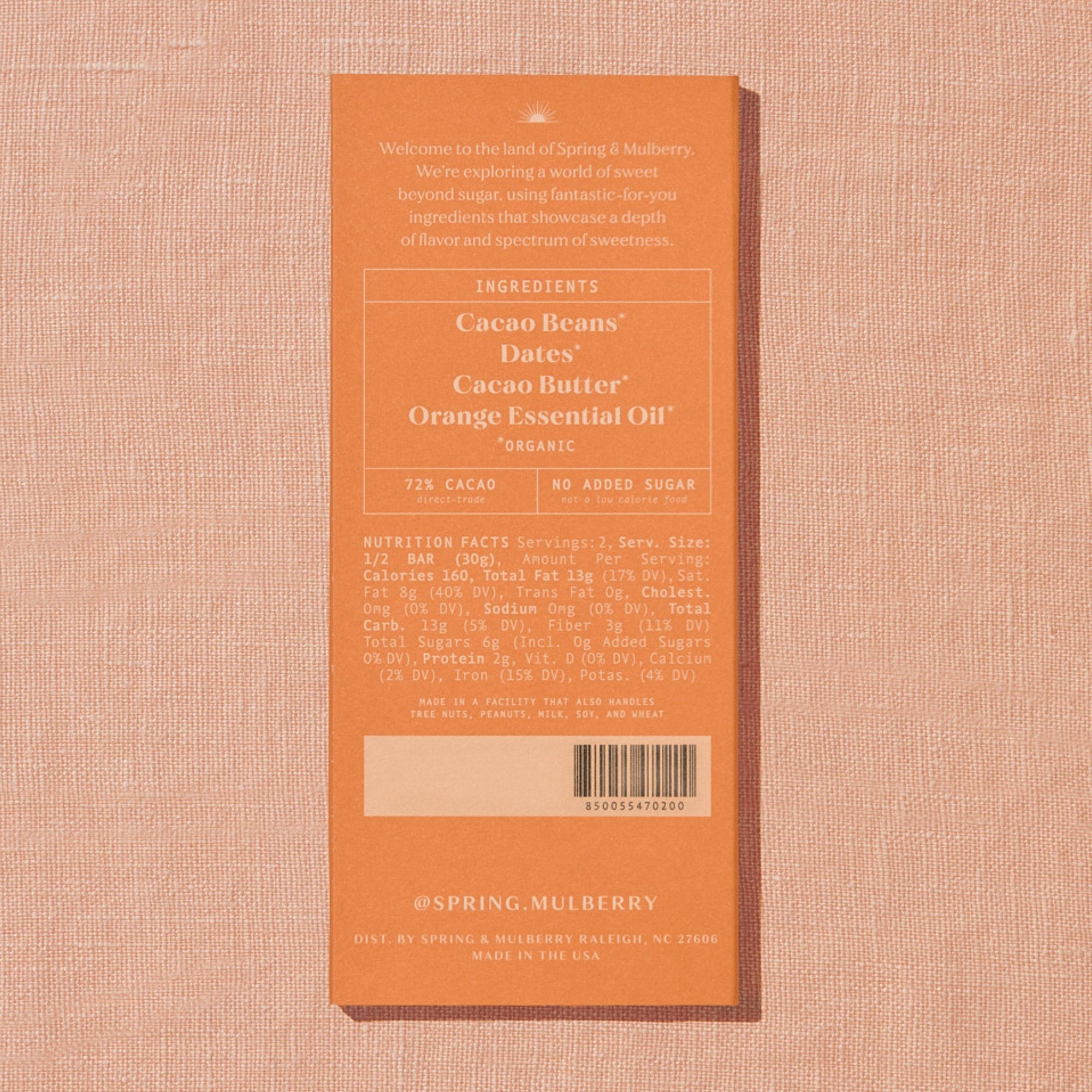 A light orange Spring & Mulberry box with its back lable showing chocolate information is laid on a warm brown background. 