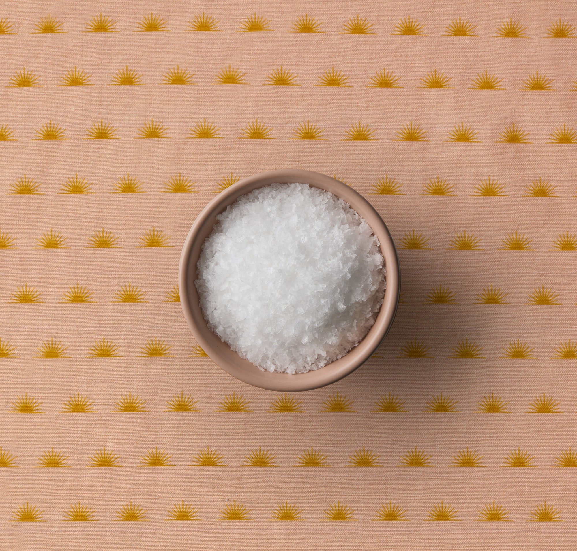 Bowl of sea salt on a sun patterned peach background