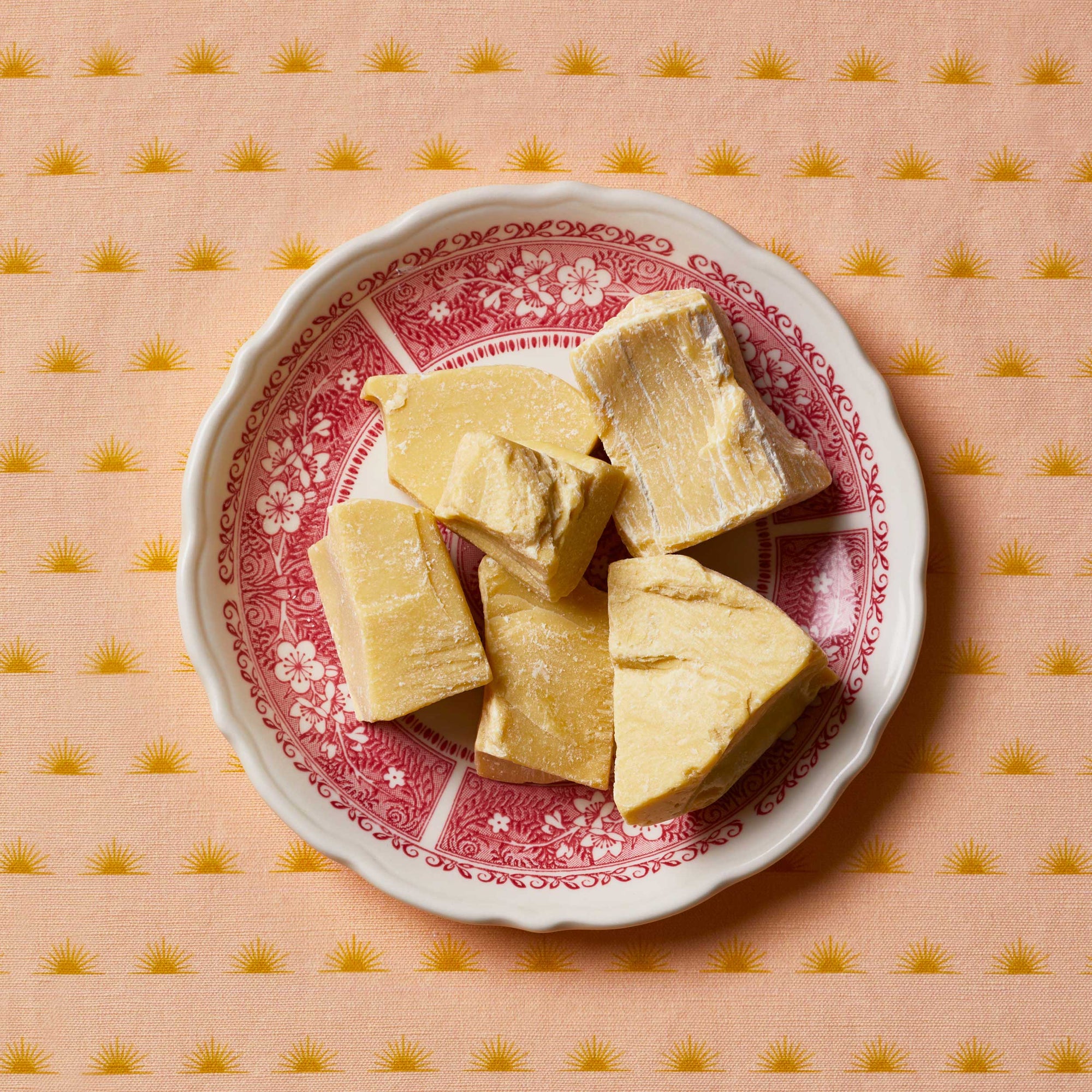 Cacao butter sitting on a white and red floral plate on top of a patterned tablecloth