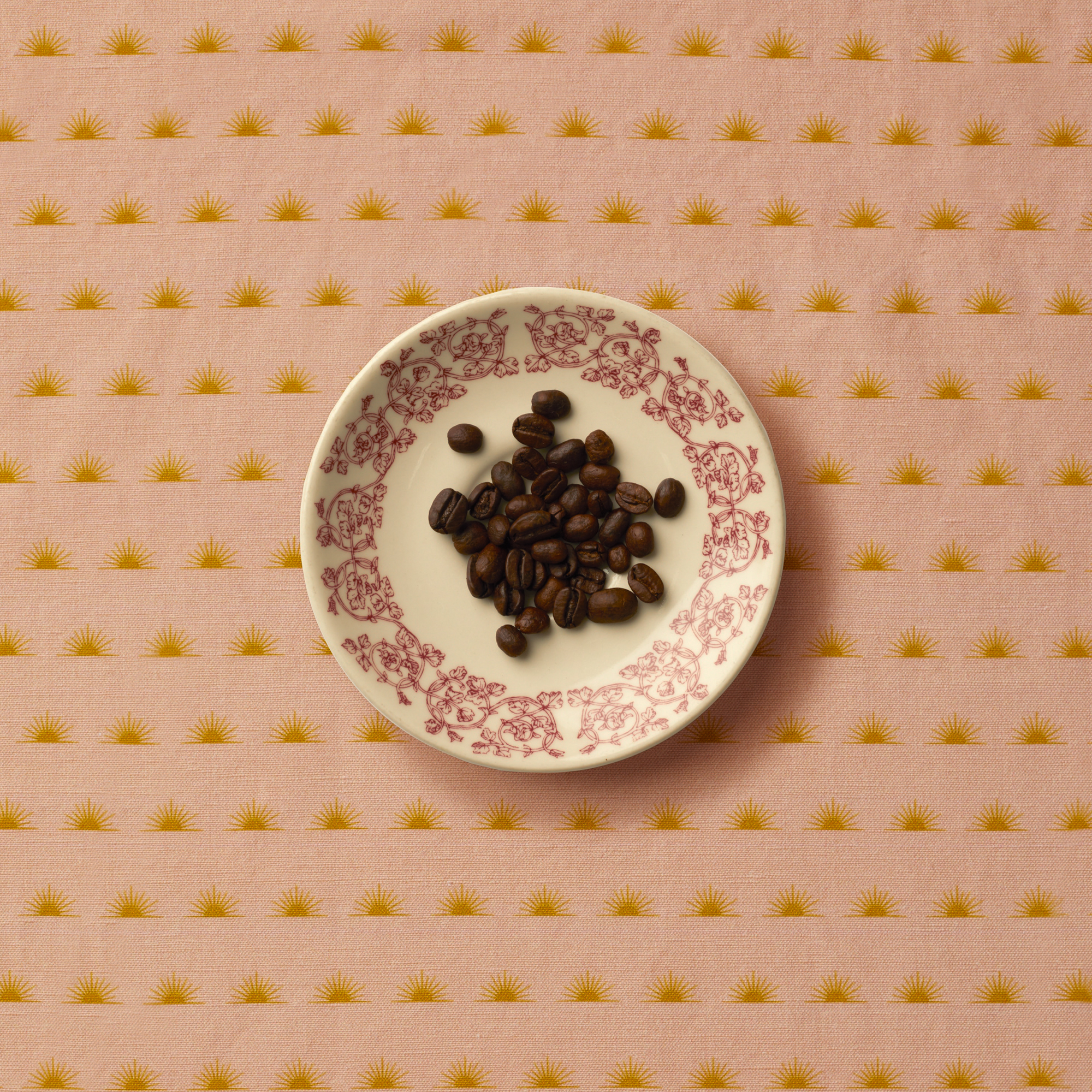 Coffee beans sitting on a floral plate on top of a patterned tablecloth