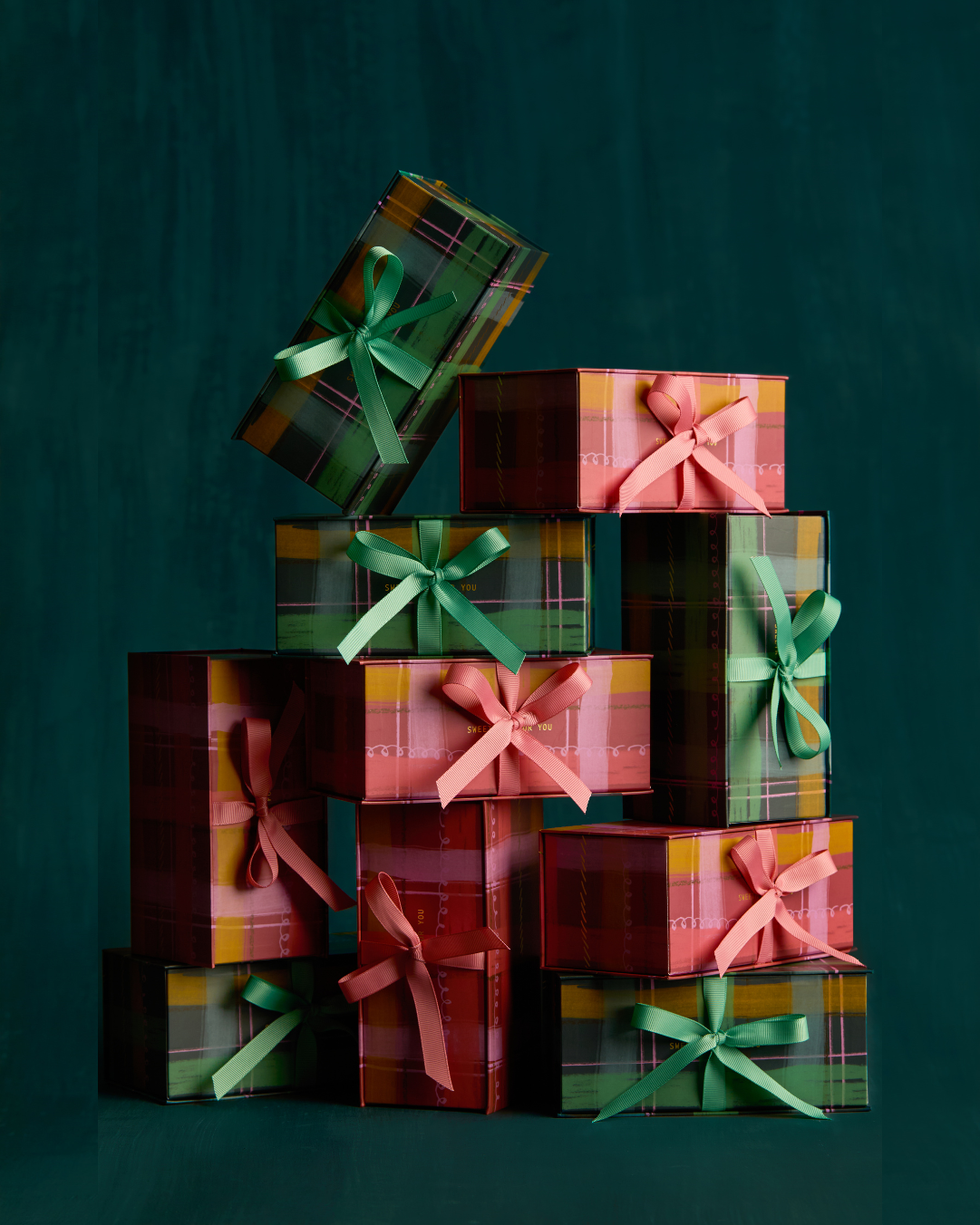 Stack of pink and green gift boxes with ribbons on a dark green background