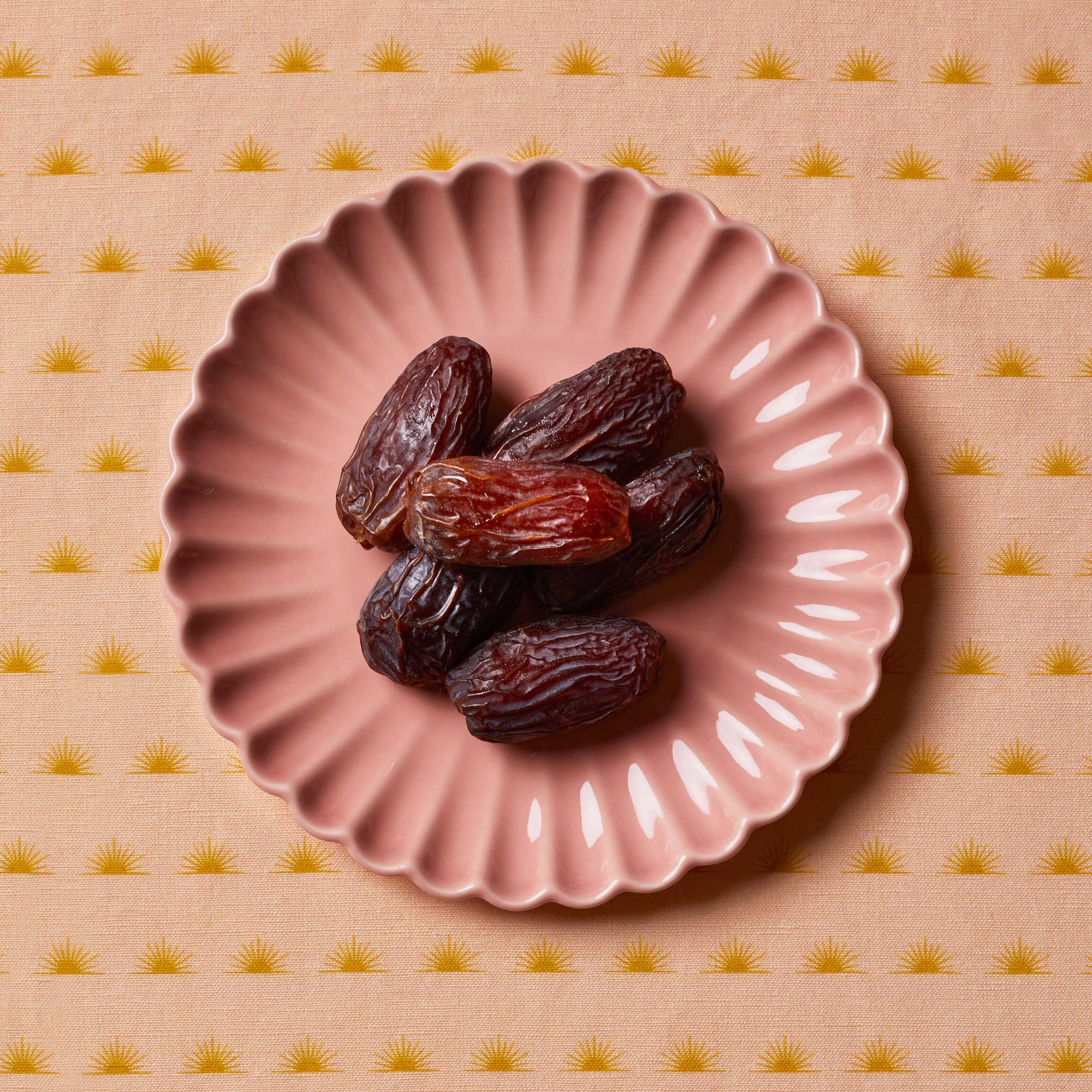 Dates sitting on a pink scalloped plate on top of a patterned tablecloth
