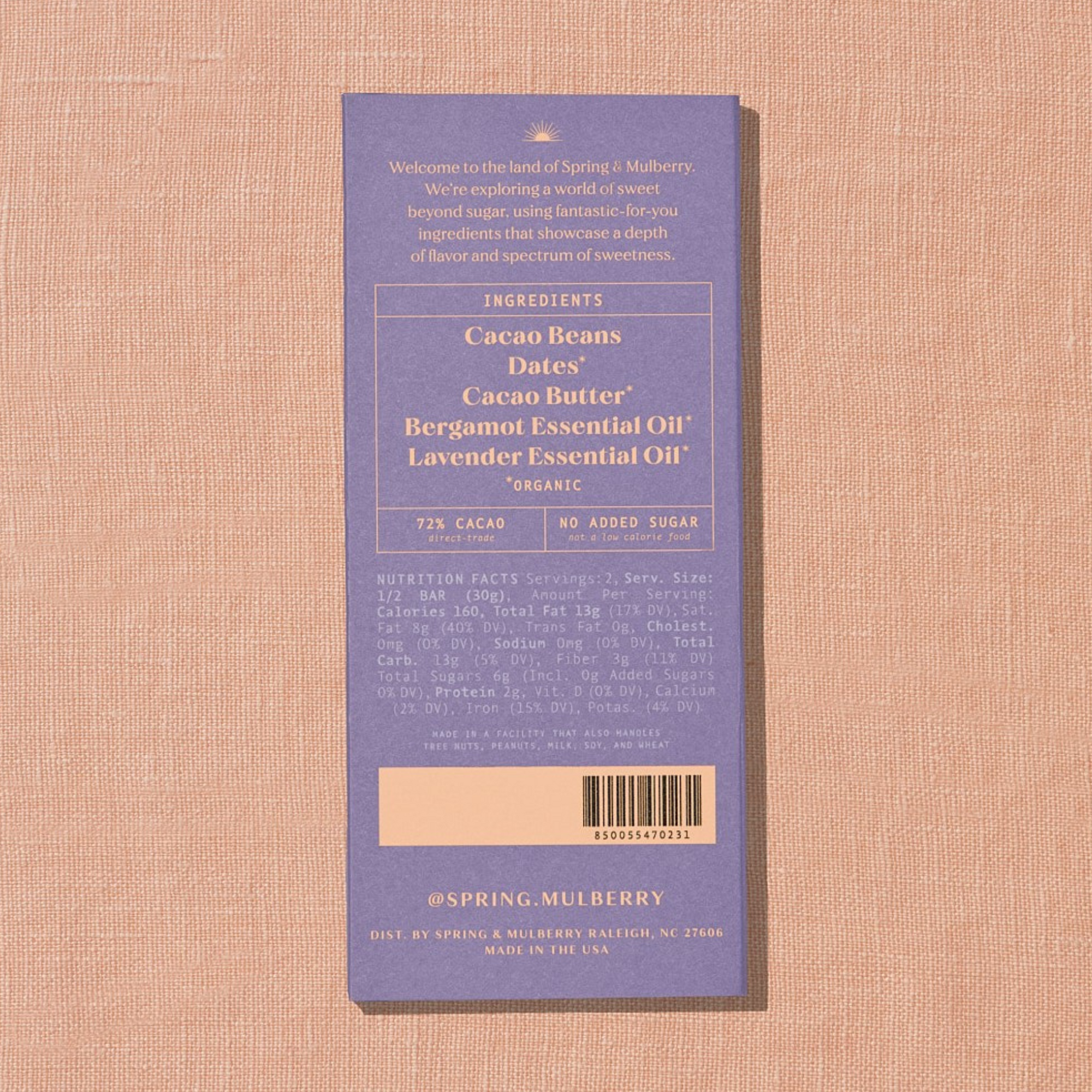 A light purple Spring & Mulberry box with its back lable showing chocolate information is laid on a warm brown background. 