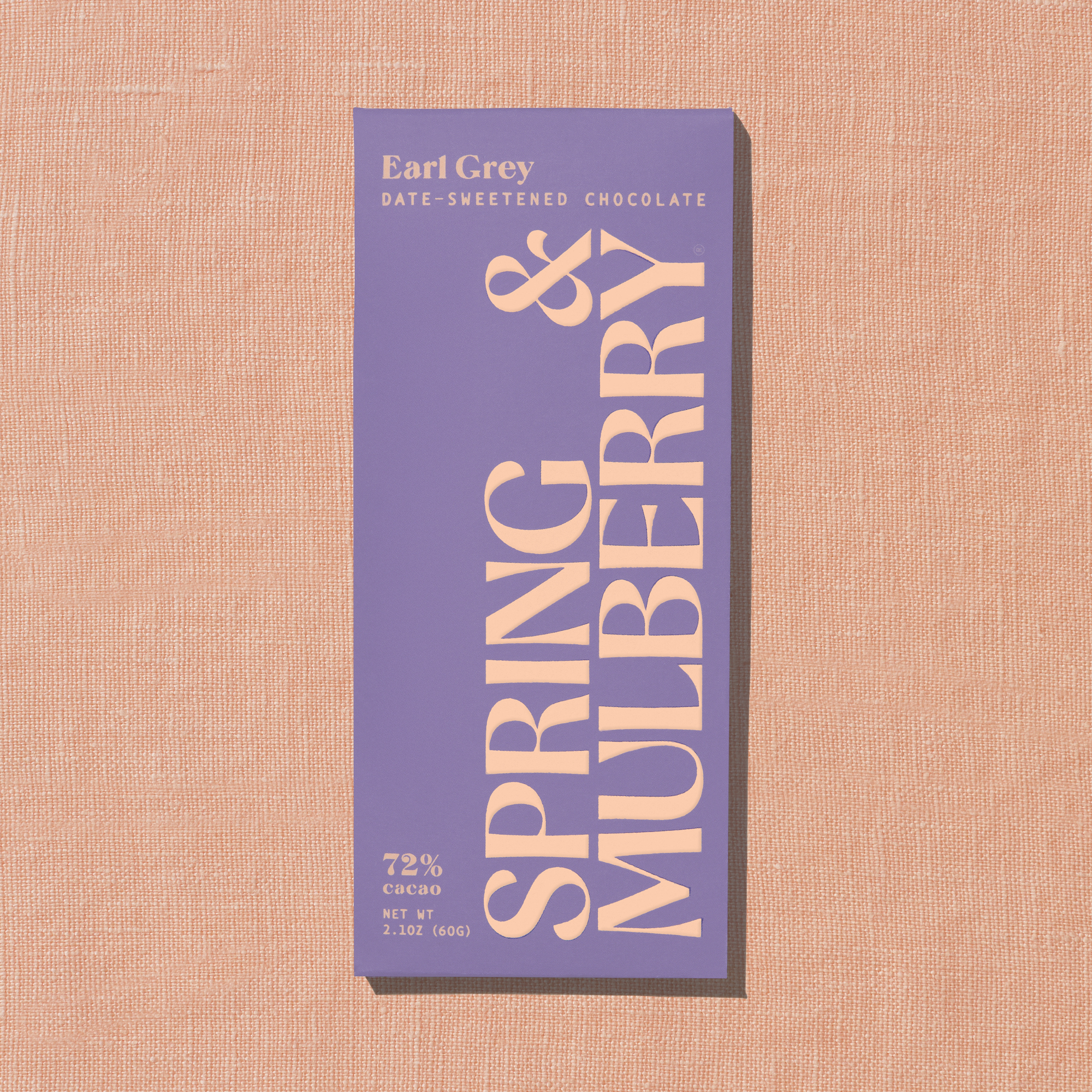 A light purple Spring & Mulberry box labeled Earl Grey date-sweetened chocolate is laid on a warm peach background. 