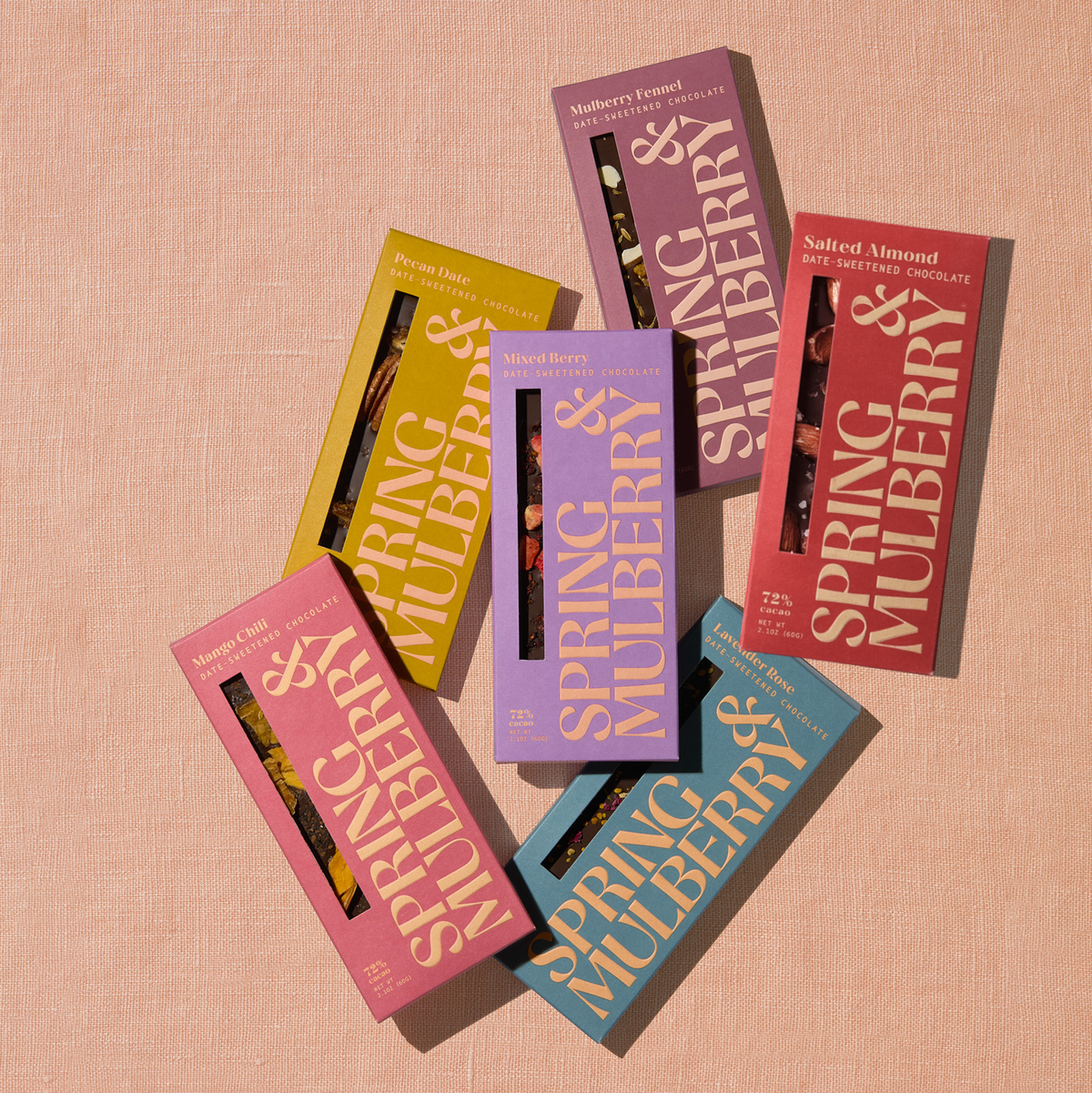 Six Spring & Mulberry dark chocolate bars arranged in an overlapping display, against a soft peach textured background.