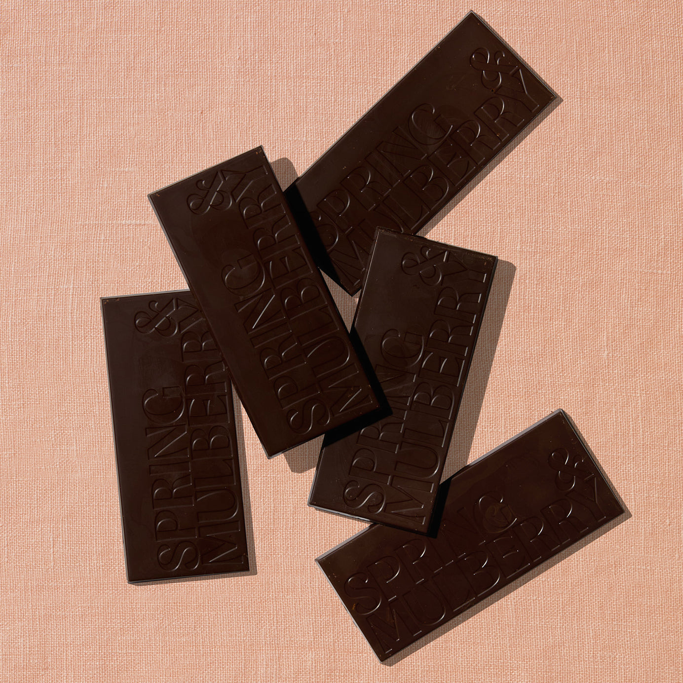 Five chocolate bars infused with essential oils, are laid out sparadically on a warm brown background.