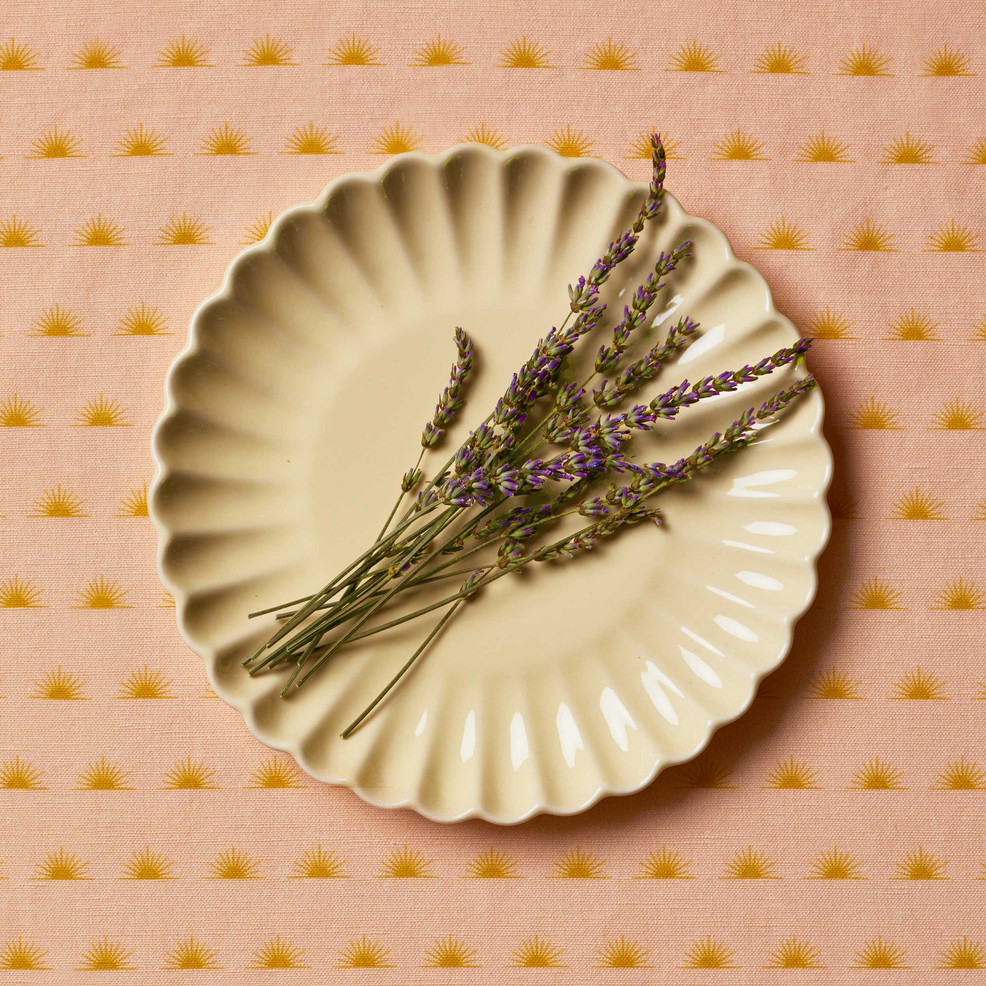 Lavender sprigs sitting on a cream scalloped plate of a patterned tablecloth
