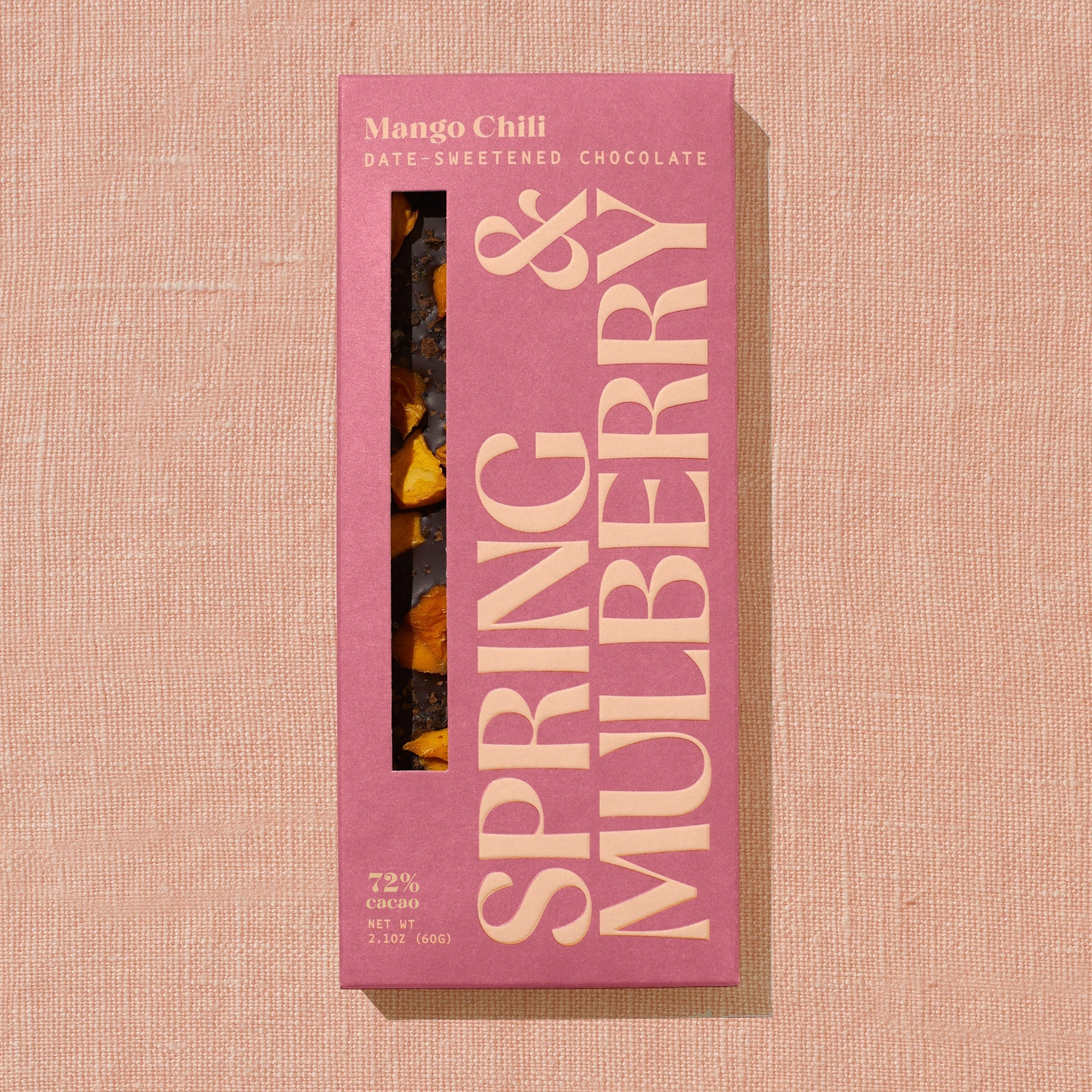 A red/orange Spring & Mulberry box labled Mango Chili date-sweetened chocolate is laid on a warm brown background. 