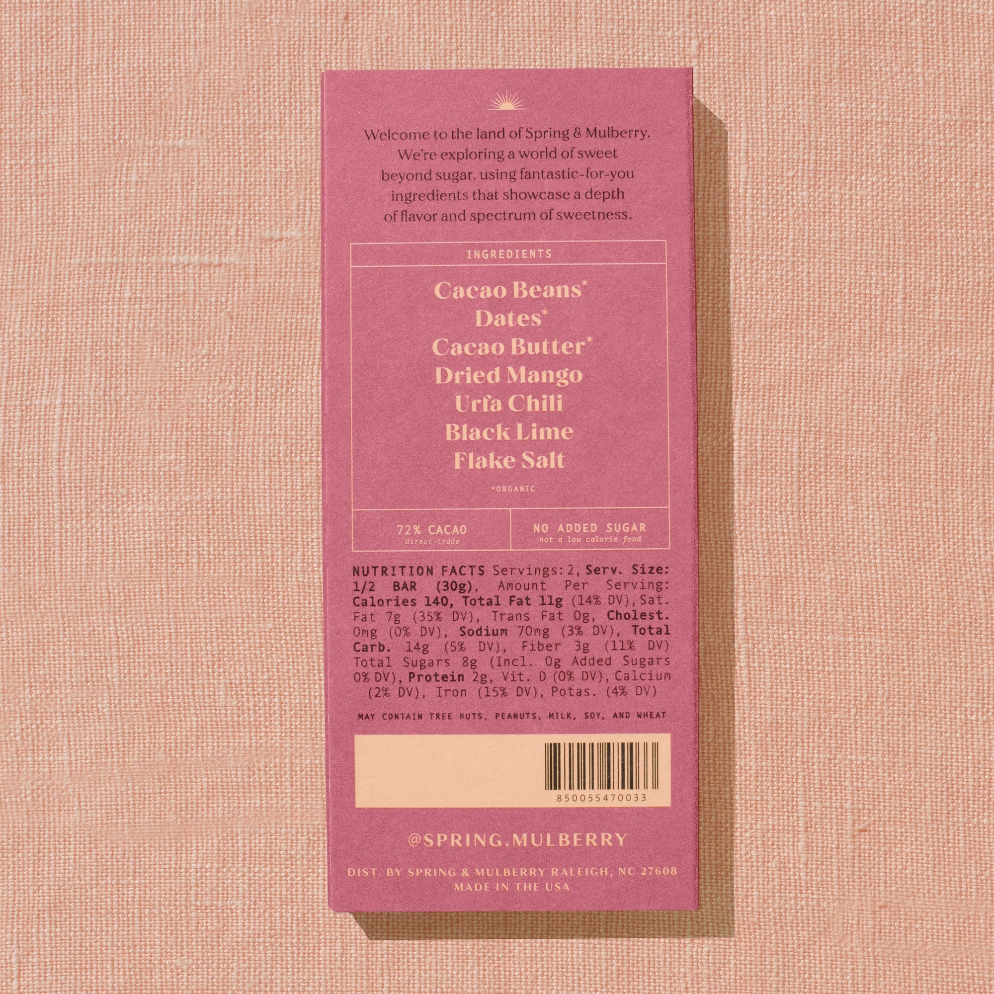 A red/orange Spring & Mulberry box with its back lable showing chocolate information is laid on a warm brown background. 