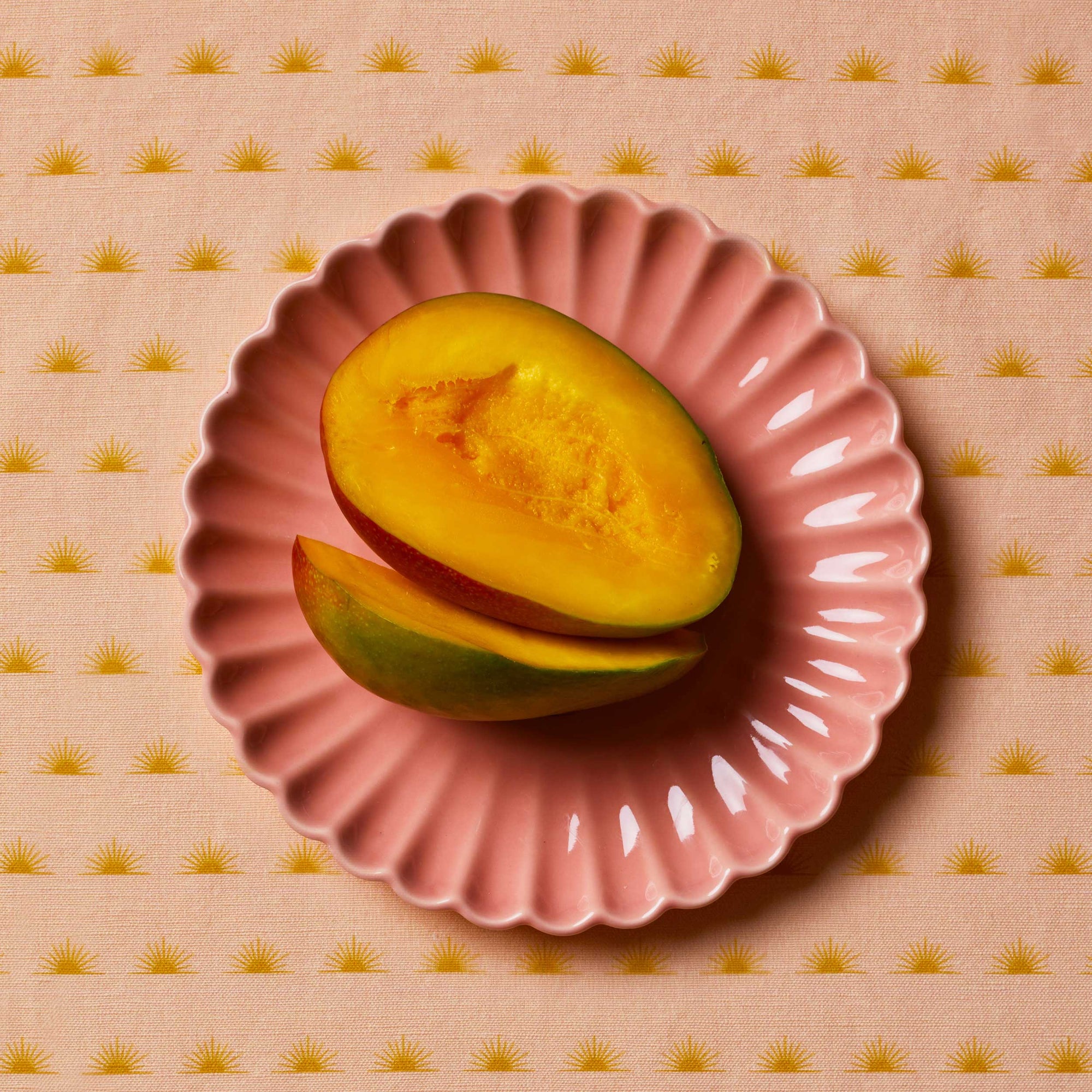Mangos sitting on a pink scalloped plate on top of a patterned tablecloth