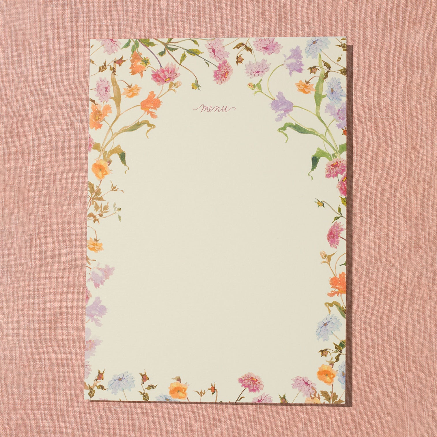 A creamy white menu card with hand-painted pink, purple, and orange floral designs placed around the edge of the card with open space in the center for menu items and laid on a pink background.
