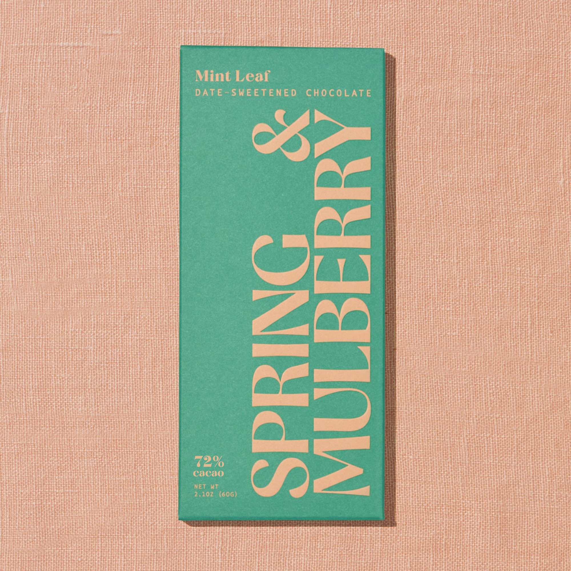 A light green Spring & Mulberry box labled Mint Leaf date-sweetened chocolate is laid on a warm brown background. 