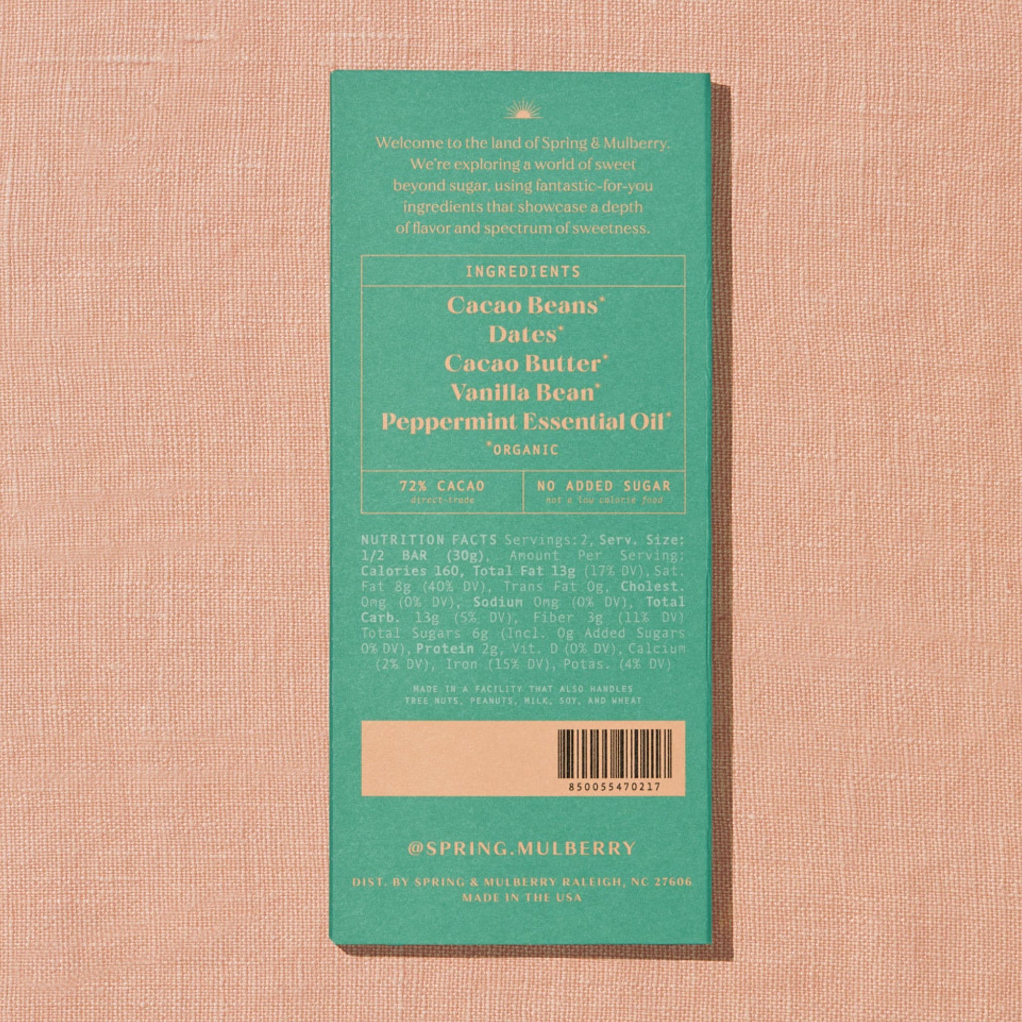 A light green Spring & Mulberry box with its back lable showing chocolate information is laid on a warm brown background. 