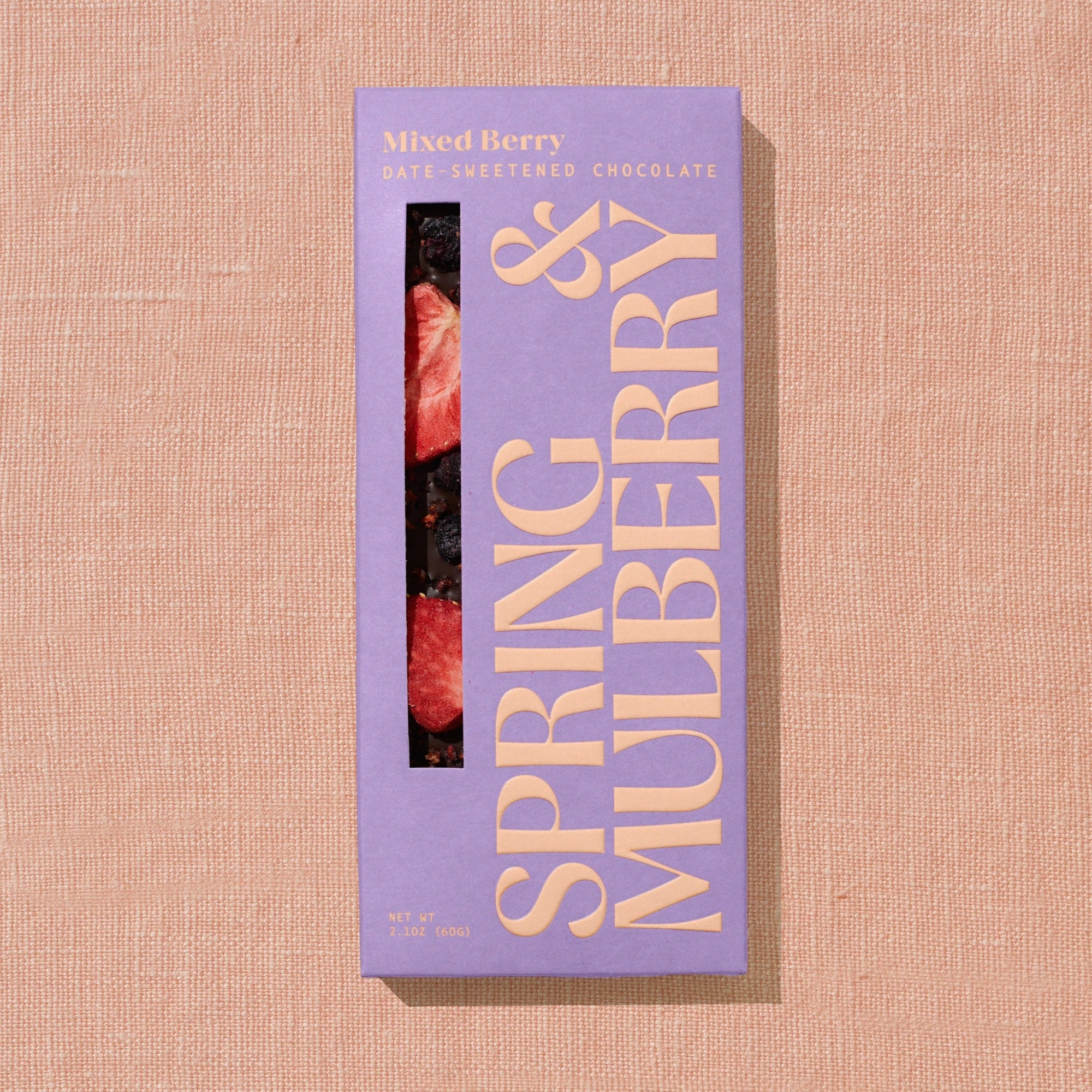 A pink/purple Spring & Mulberry box labled Mixed Berry date-sweetened chocolate is laid on a warm brown background. 