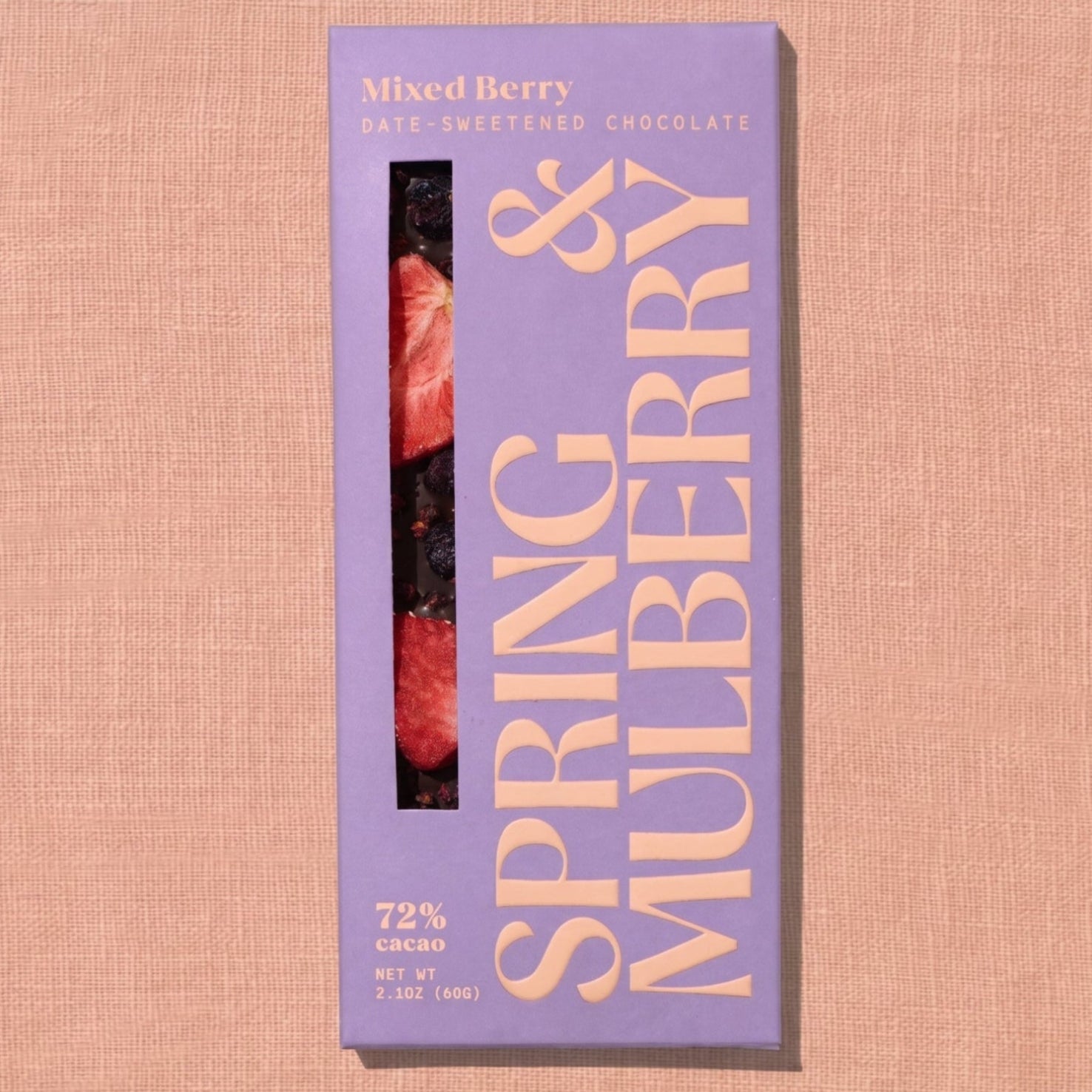 A pink/purple Spring & Mulberry box labled Mixed Berry date-sweetened chocolate is laid on a warm brown background. 