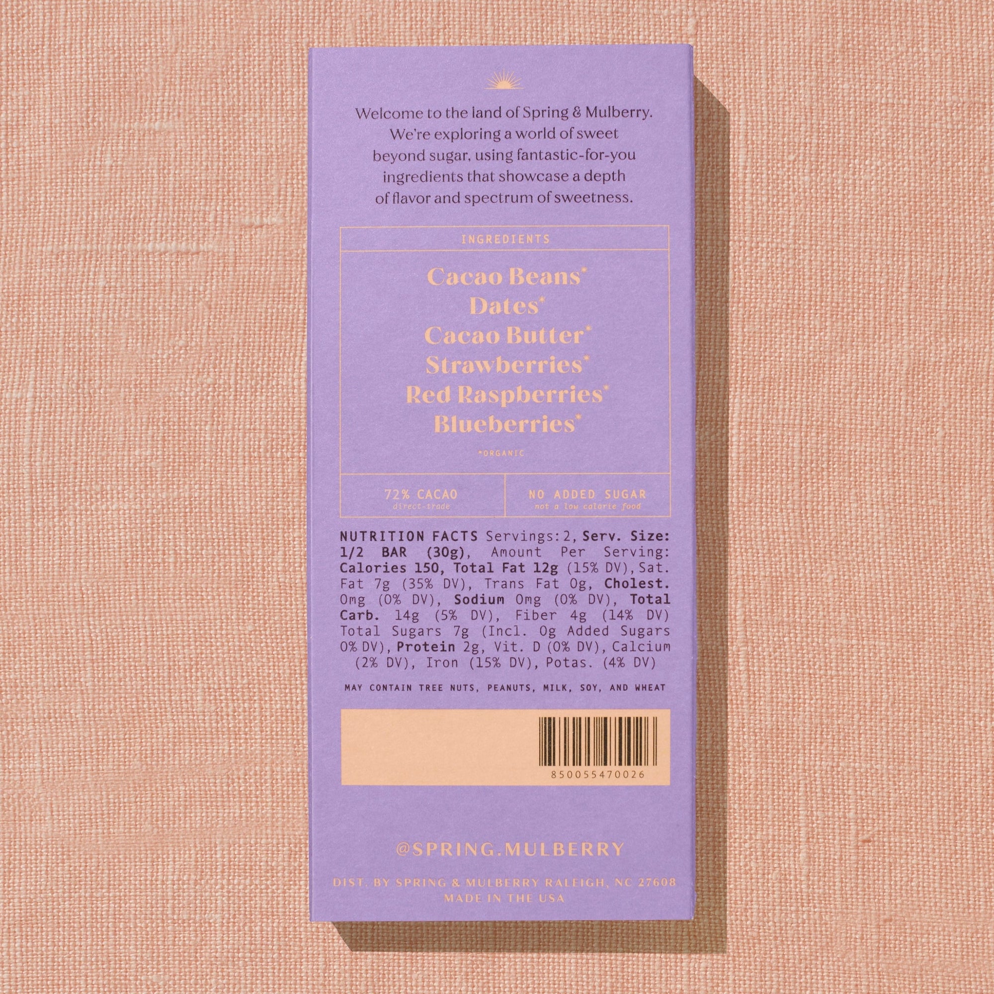 A pink/purple Spring & Mulberry box with its back lable showing chocolate information is laid on a warm brown background. 