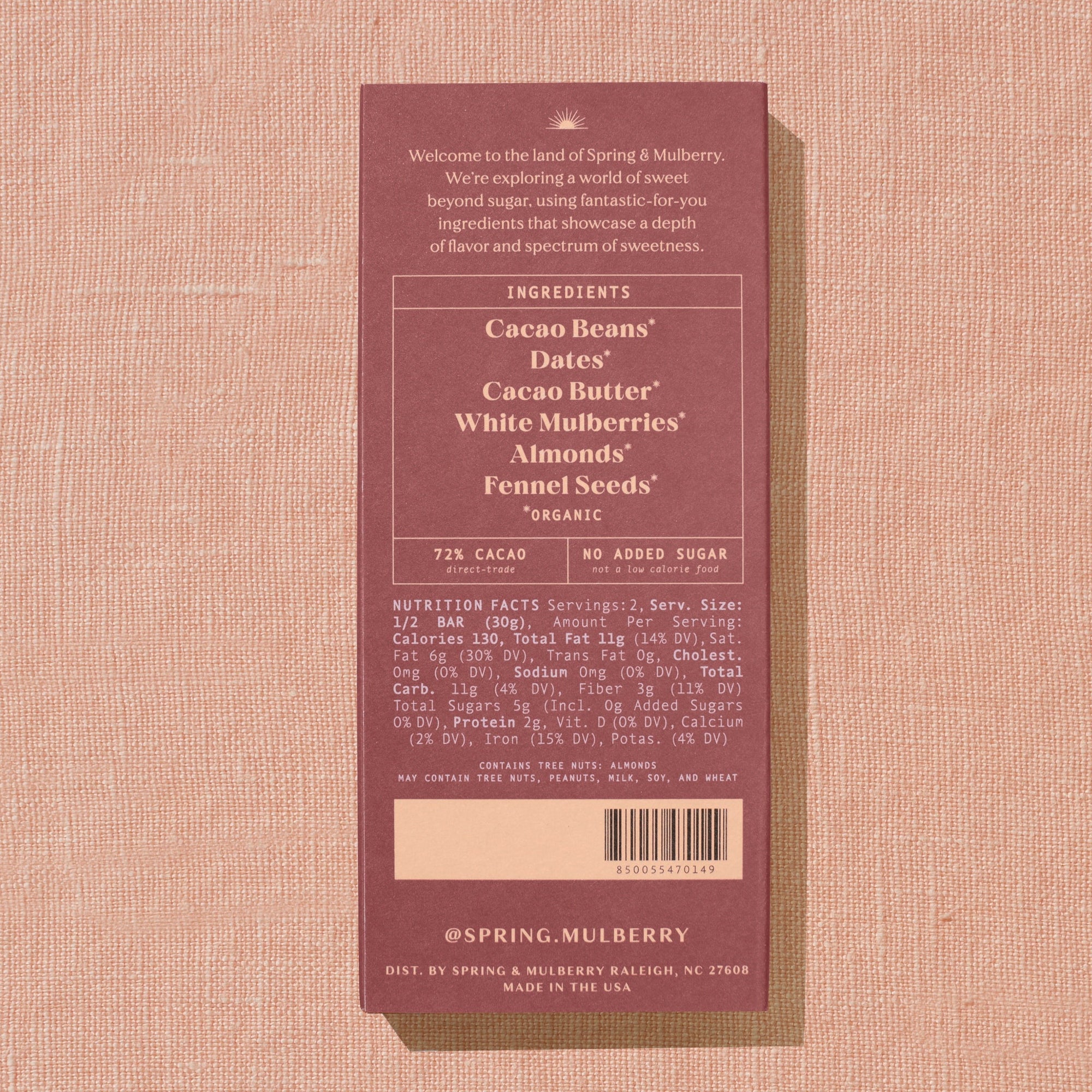 A brick red Spring & Mulberry box with its back lable showing chocolate information is laid on a warm brown background. 