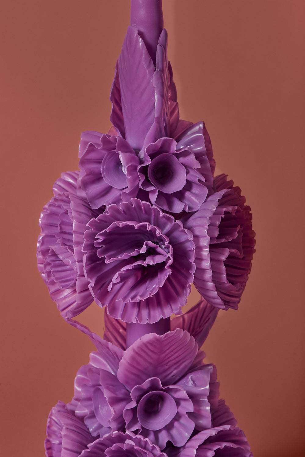 Close up of the intricate lilac candle with wax flowers and leaves on a brown background 