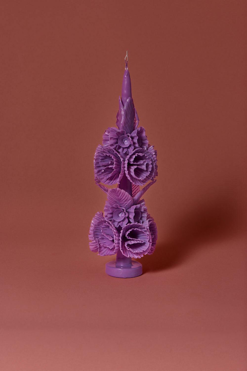 Intricate lilac candle with wax flowers and leaves on a brown background 