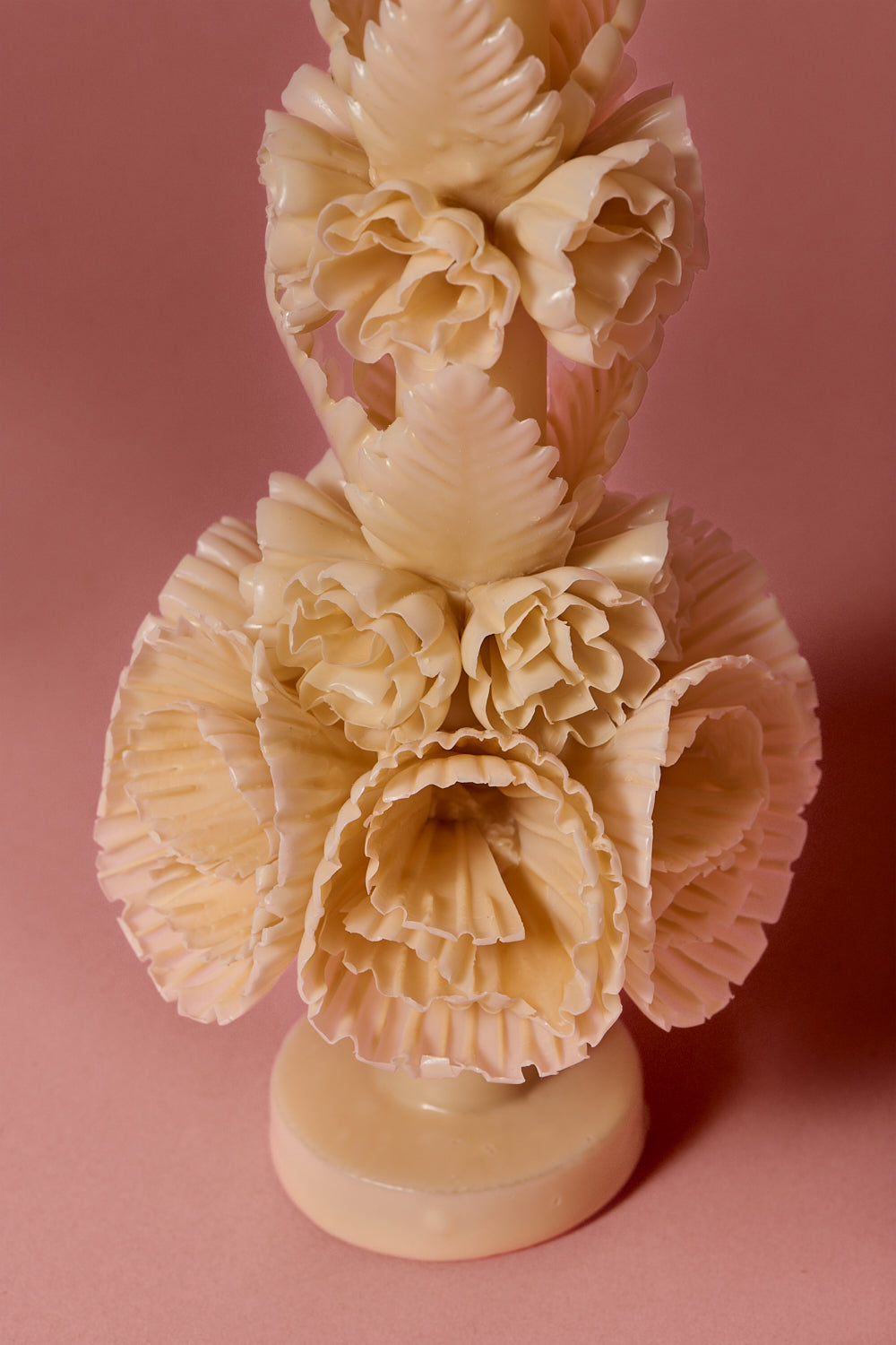  Close up view of the intricate peach colored candle, with wax flowers and leaves on a brown background