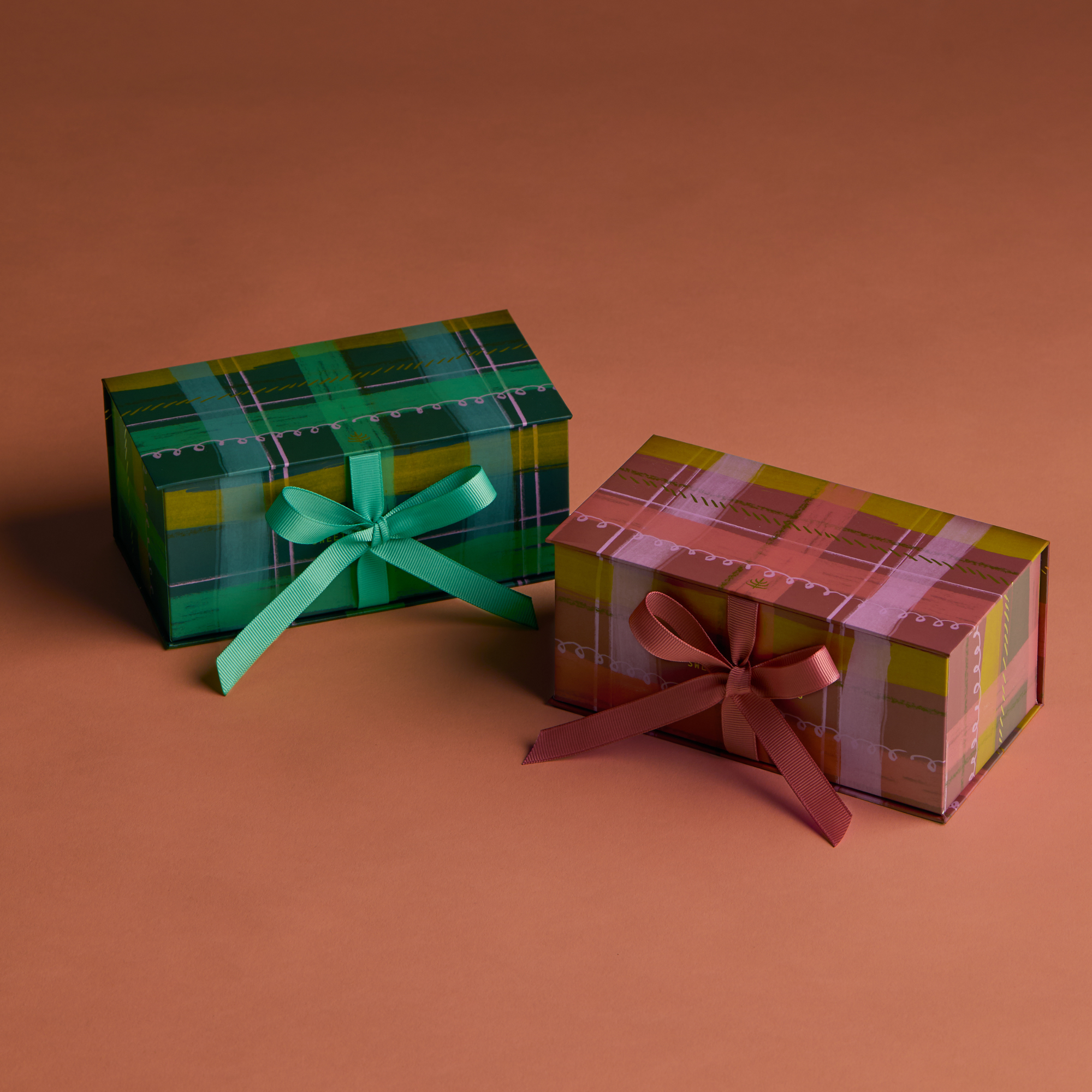 Two gift boxes with colorful plaid patterns and tied ribbons on a warm brown background.