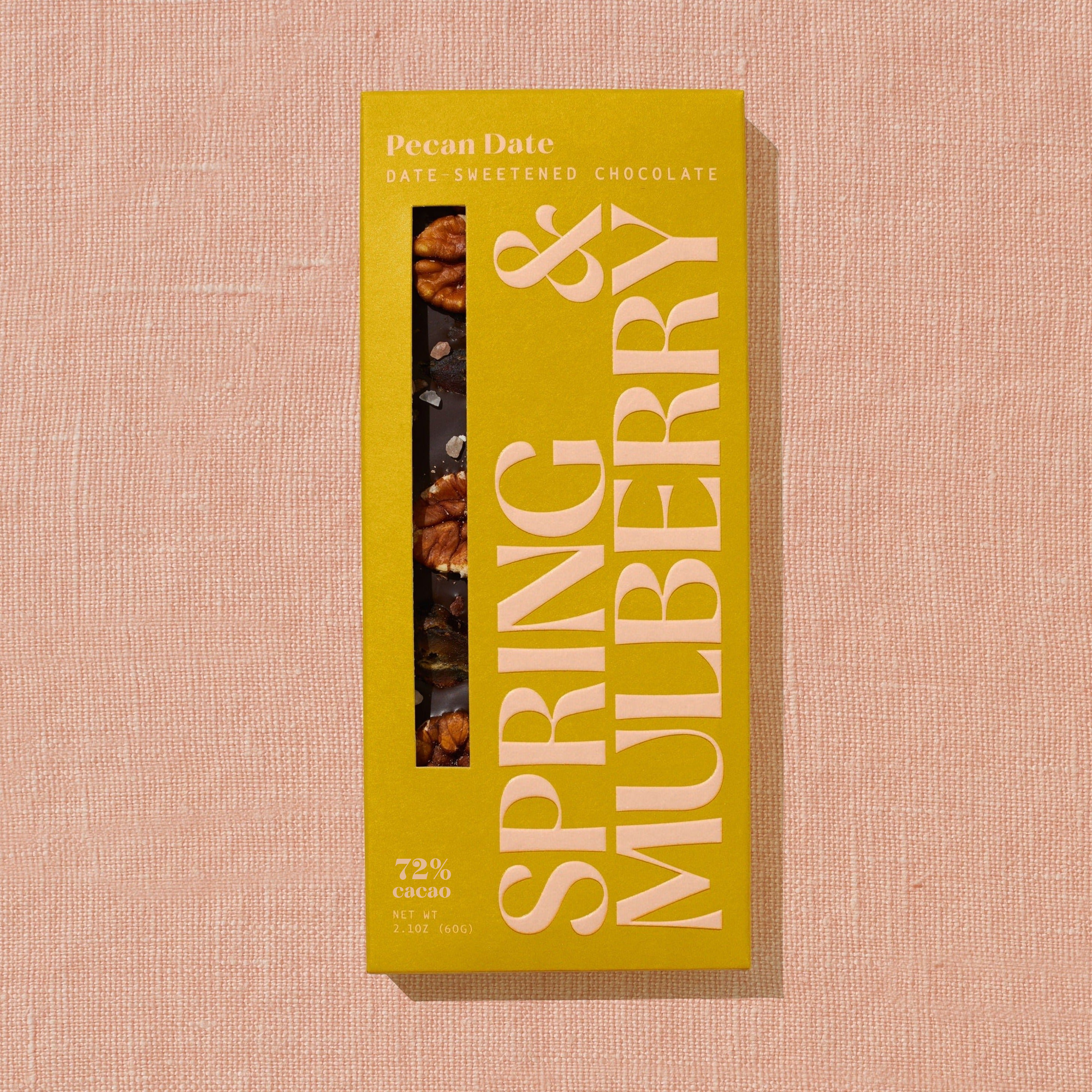 A bright golden Spring & Mulberry box labled Pecan Date date-sweetened chocolate is laid on a warm brown background. 