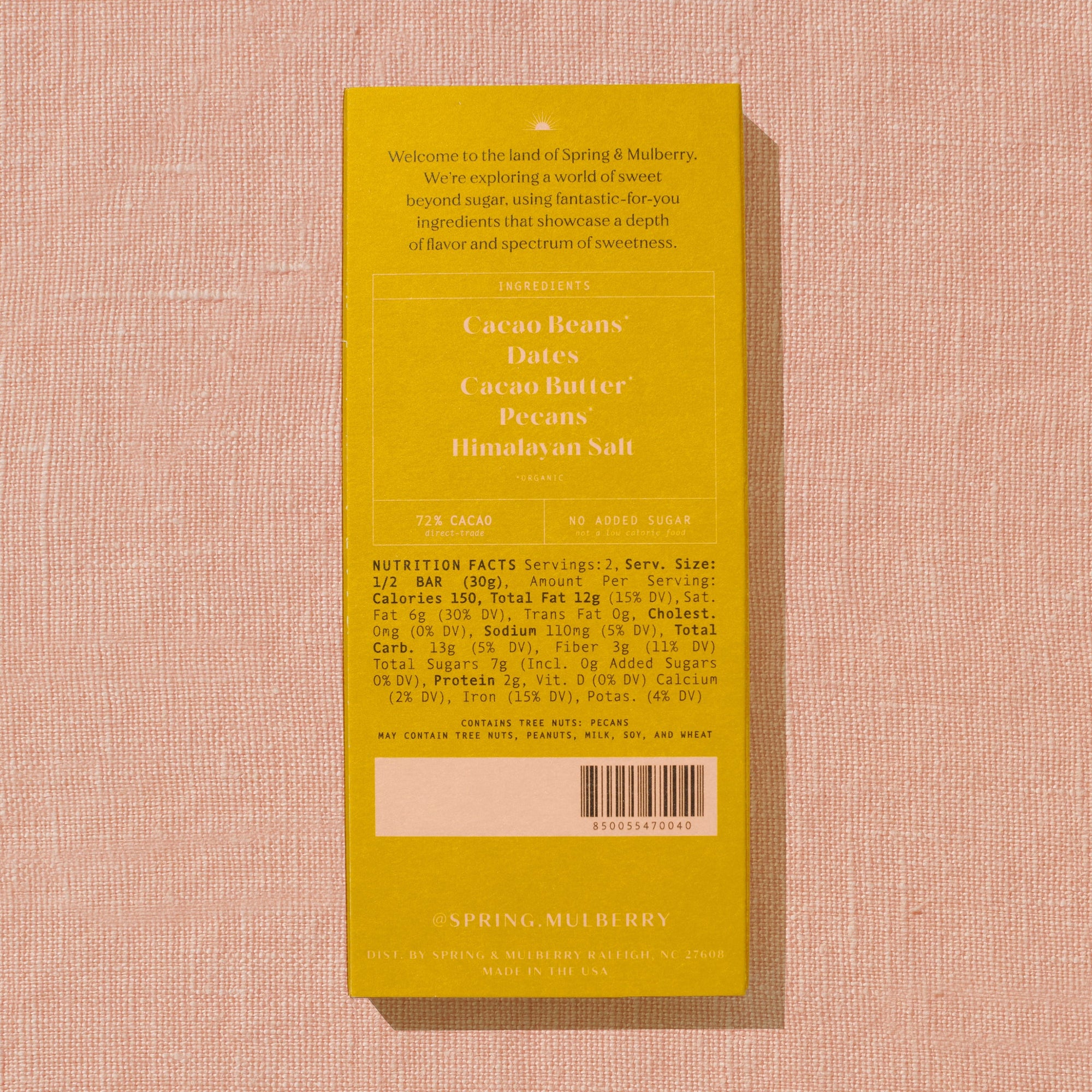 A bright golden Spring & Mulberry box with its back lable showing chocolate information is laid on a warm brown background. 