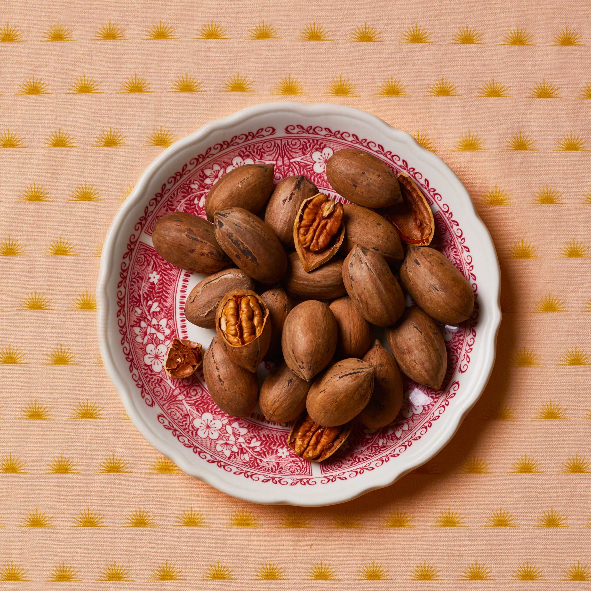 Pecans sitting in a white and red floral bowl on top of a patterned tablecloth
