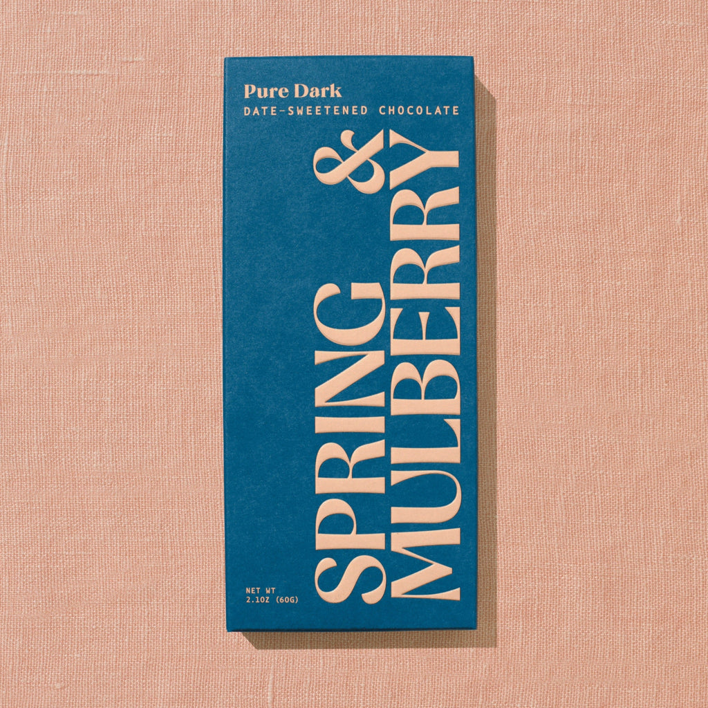 A dark blue Spring & Mulberry box labeled Pure Dark date-sweetened chocolate on a warm brown background.