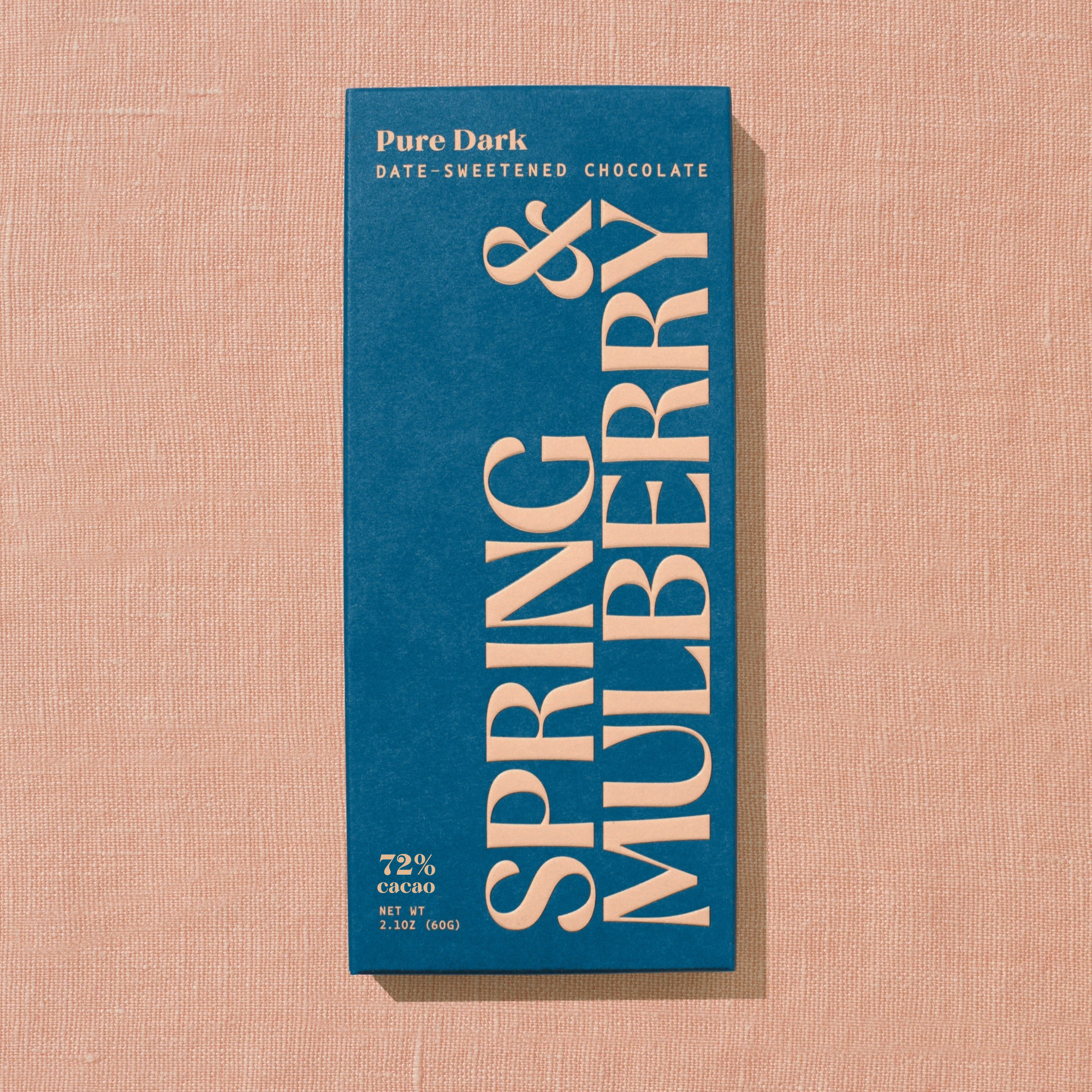 A dark blue Spring & Mulberry box labled Pure Dark date-sweetened chocolate is laid on a warm brown background. 