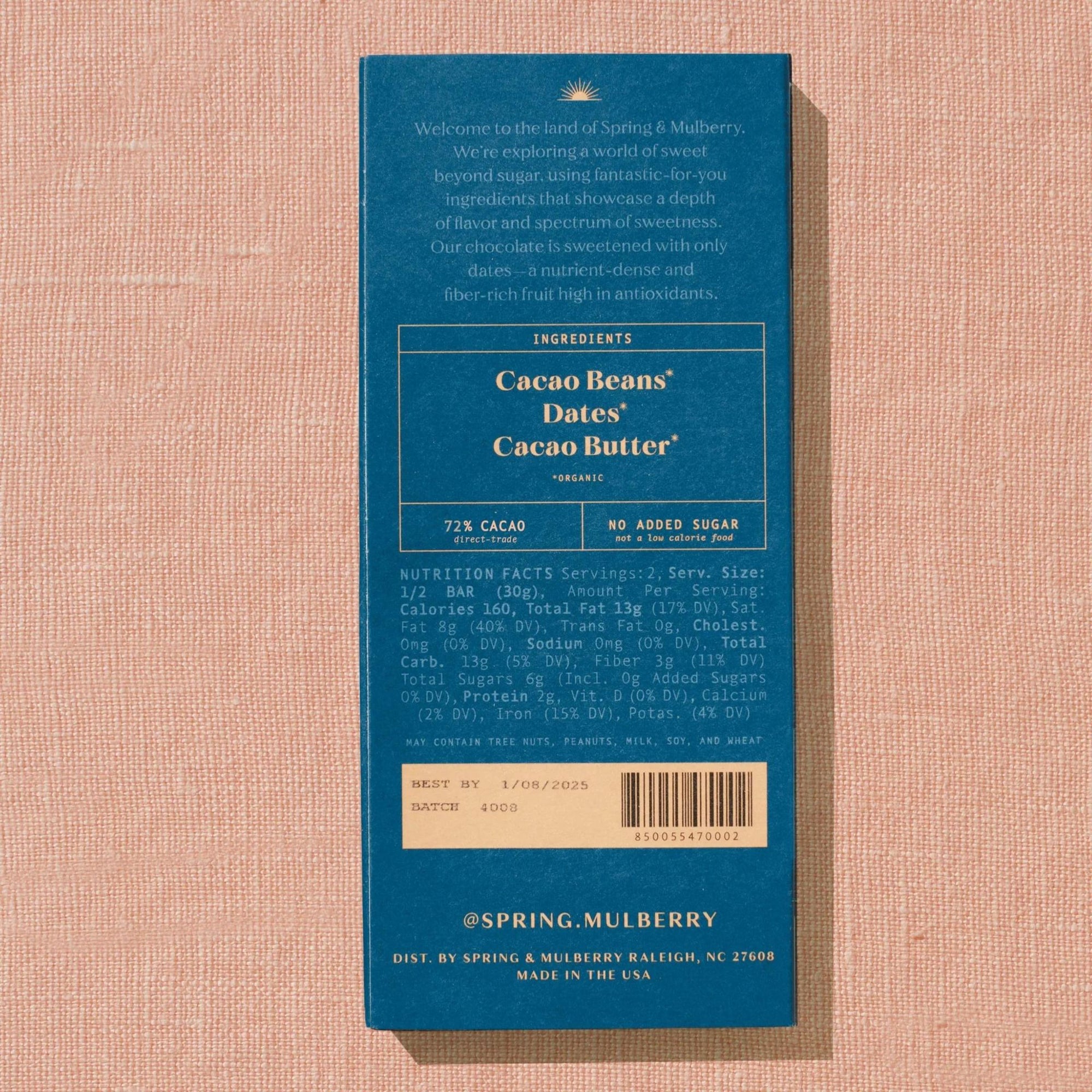 A dark blue Spring & Mulberry box is displaying it's back lable showing chocolate information is laid on a warm brown background. 