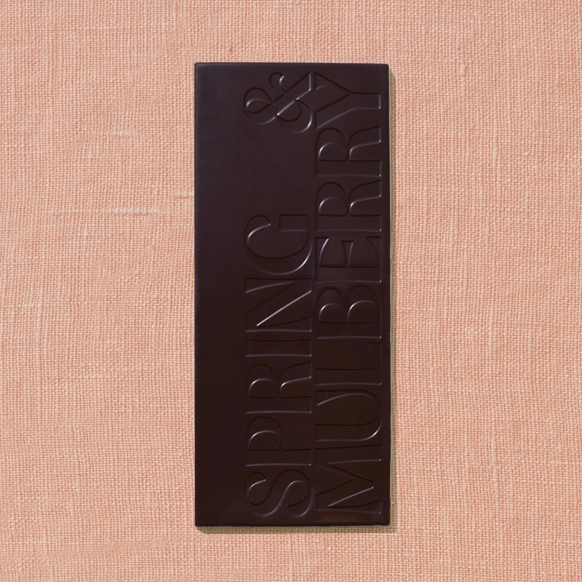 Spring & Mulberry Pure Dark bar featuring the brand’s embossed logo, on a soft peach textured background.